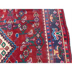 Persian Herati crimson ground rug, the busy field decorated with a central lozenge medallion surrounded by interlocking Herati motifs, the indigo guard band with repeating palmette and stylised plant motifs