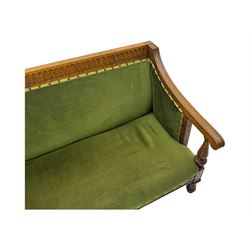 Late Victorian walnut framed sofa, rectangular backrest with carved detailing and central motif, upholstered in olive green fabric with brass studded trim and patterned front rail, scrolled fluted arms supported by turned uprights terminating in bun feet