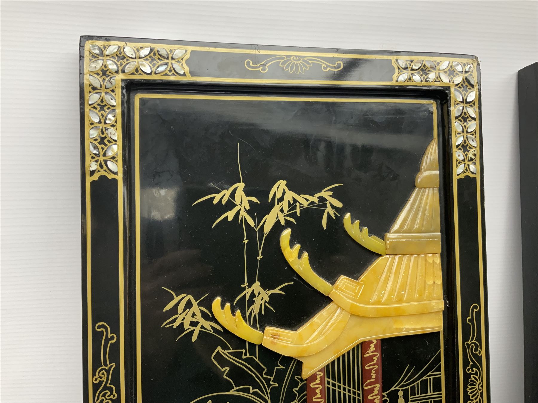 Two 20th century Chinese lacquered wall plaques, decorated in relief with female figures playing instruments beneath a pagoda, within gilt and mother of pearl inlaid borders, H92cm