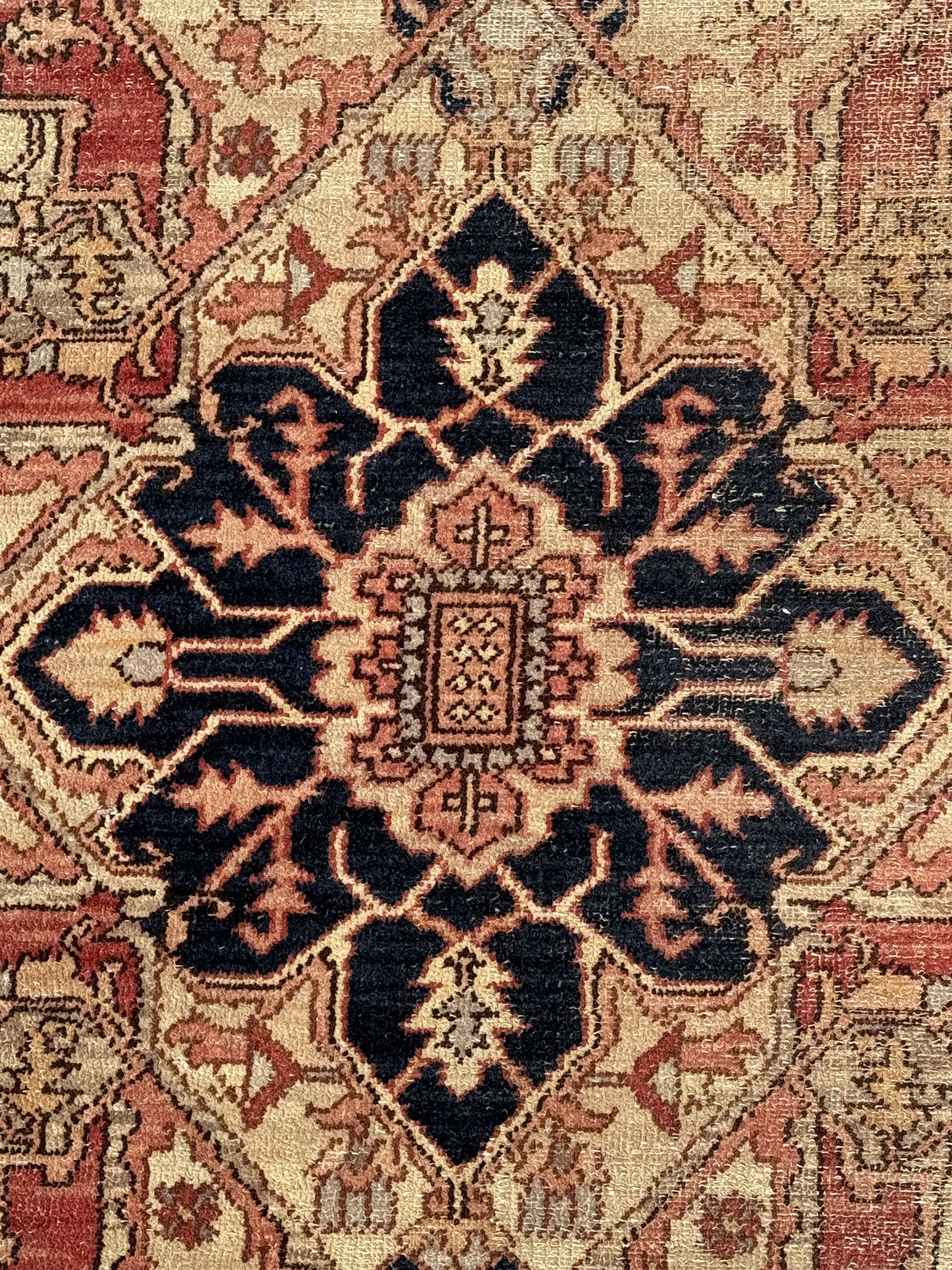 Persian Heriz design rug with red ground, the field featuring a central medallion with floral and geometric motifs, surrounded by ivory spandrels, the main border showcasing a series of floral patterns on a dark blue ground