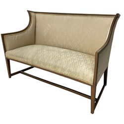 Edwardian mahogany framed two-seat sofa, curved wingback frame with satinwood banding, upholstered in beige fabric, on square tapering supports united by H-stretcher 