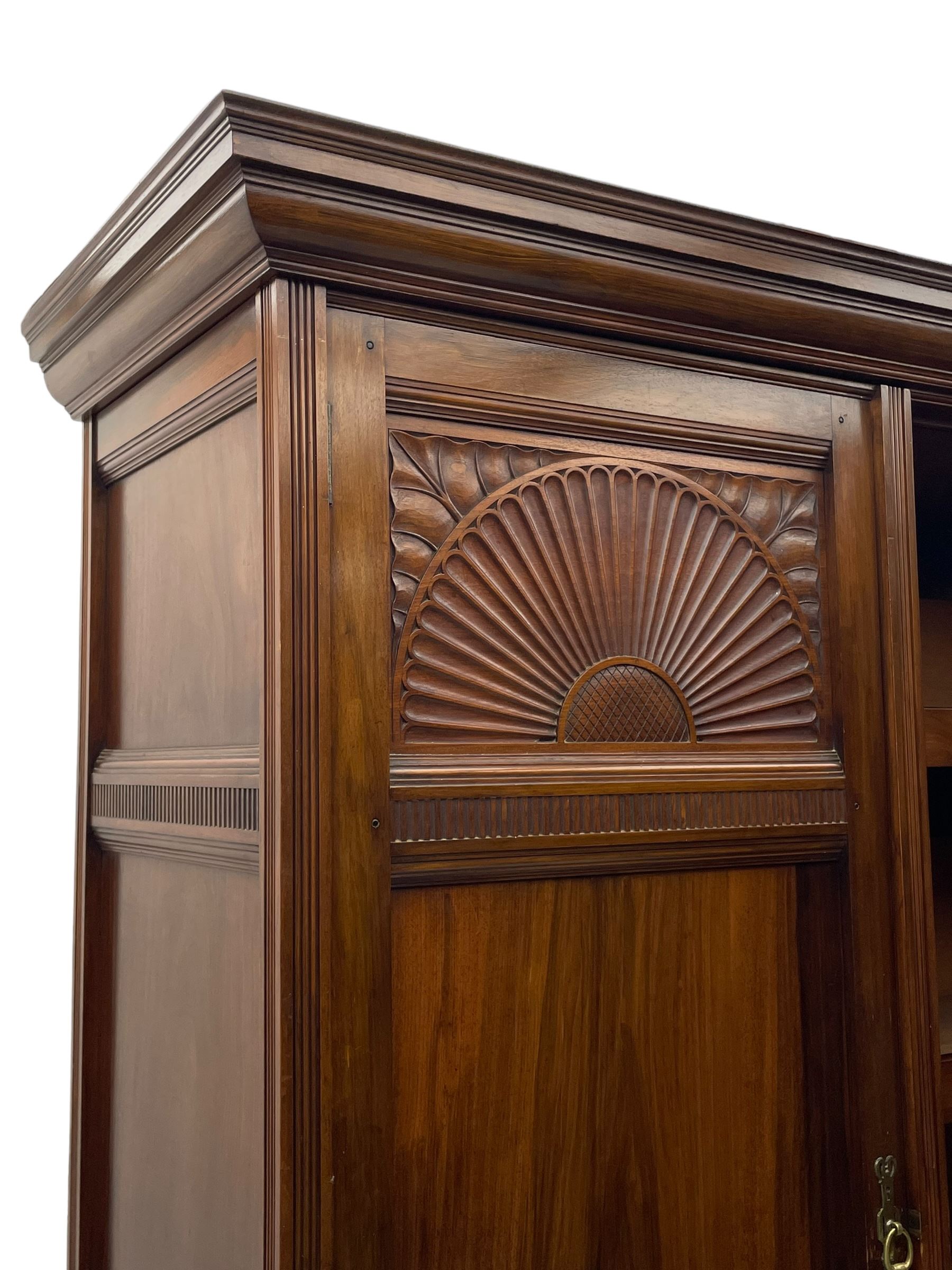 Late Victorian walnut triple wardrobe, projecting moulded cornice over central bevelled mirror door and flanking panelled doors, the top panels carved with fluted fans and stylised leaf motifs, the interior fitted with three linen slides, two drawers and hanging space, two long drawers to base, reed moulded uprights and vertical fluted horizontal rails 