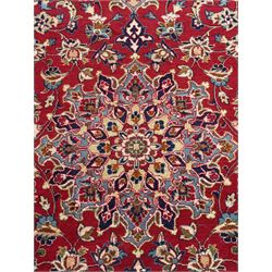 Persian Kashan red ground rug, the field decorated with a central floral medallion surrounded buy scrolling vine motifs and palmettes, the main border featuring a series of stylised floral motifs against a dark blue ground, enclosed by multiple guard stripes with alternating floral and geometric designs