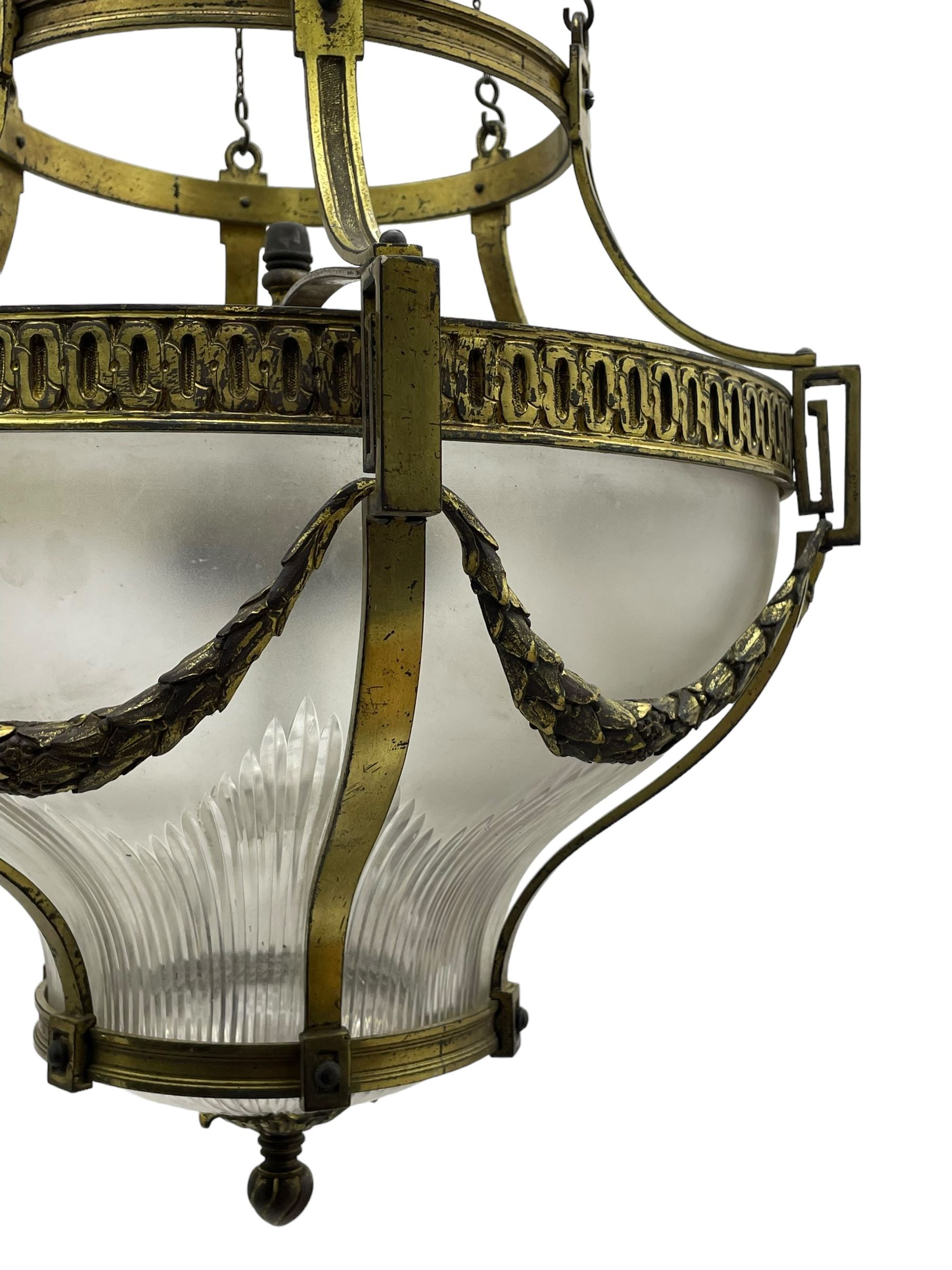 Edwardian brass ceiling light of circular bulbous form, moulded upper band over a guilloche cast central band united by shaped strapping, decorated with fruiting foliage festoons, fitted with frosted and vertical bevelled glass bowl, acanthus cast finial 