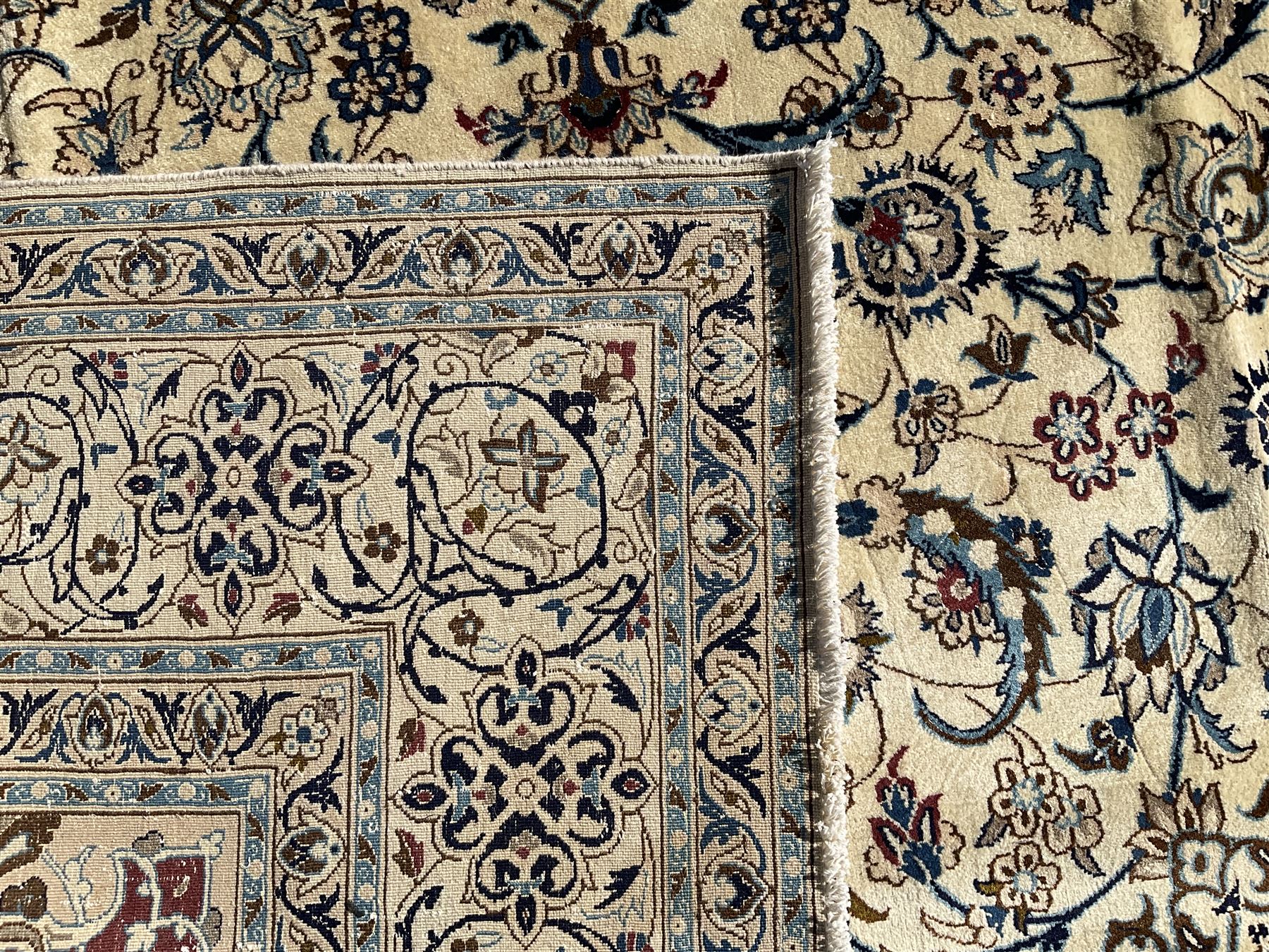 Persian Nain ivory ground carpet, central indigo medallion, the busy floral field decorated with scrolling vines and flower heads in shades of blue, beige, and red, wide guarded border with repeating palmettes and foliate motifs