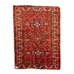 Persian Hamadan rug, red ground with overall geometric design, the field with three extended lozenges, decorated with geometric and stylised flower head motifs, the border and guards decorated with repeating geometric motifs