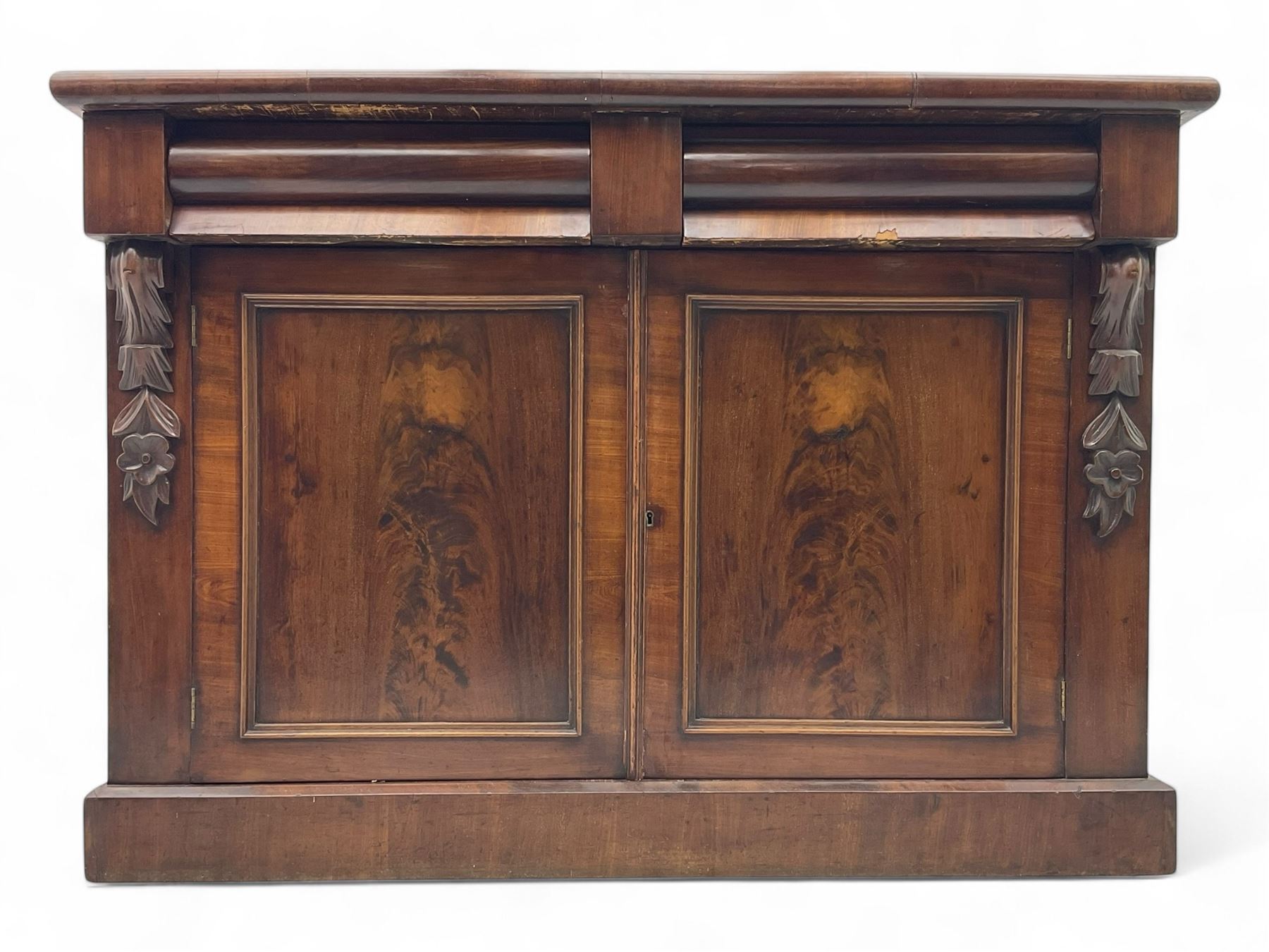 Mid 19th century mahogany sideboard, rectangular top over two frieze drawers with rounded edges, flanked by floral carved corbels, over two panelled cupboard doors, raised on a plinth base