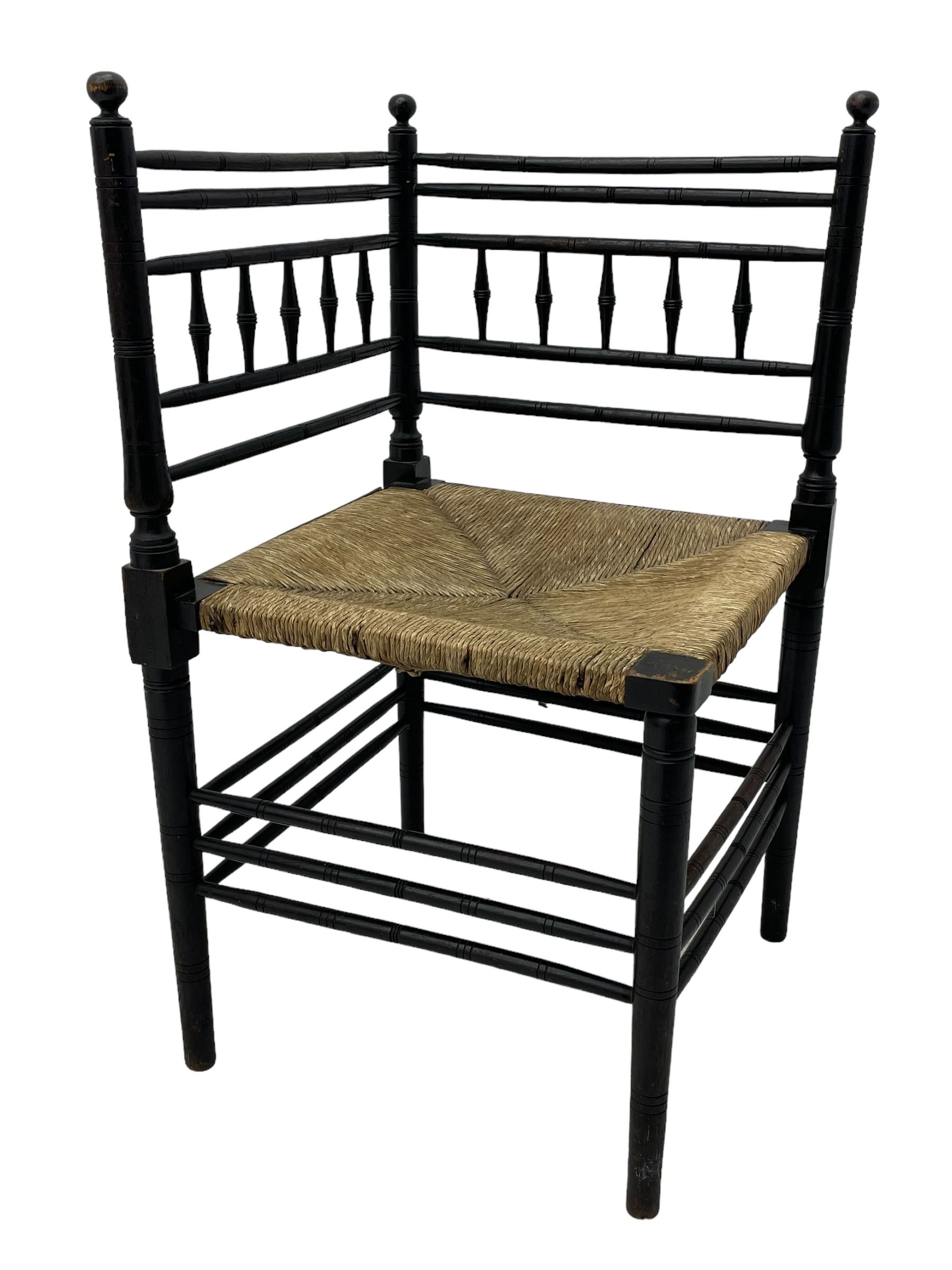 In the manner of William Morris - Arts & Crafts period corner chair, swell turned horizontal rails with balustrade back, rush seat on ring turned supports, black paint finish 