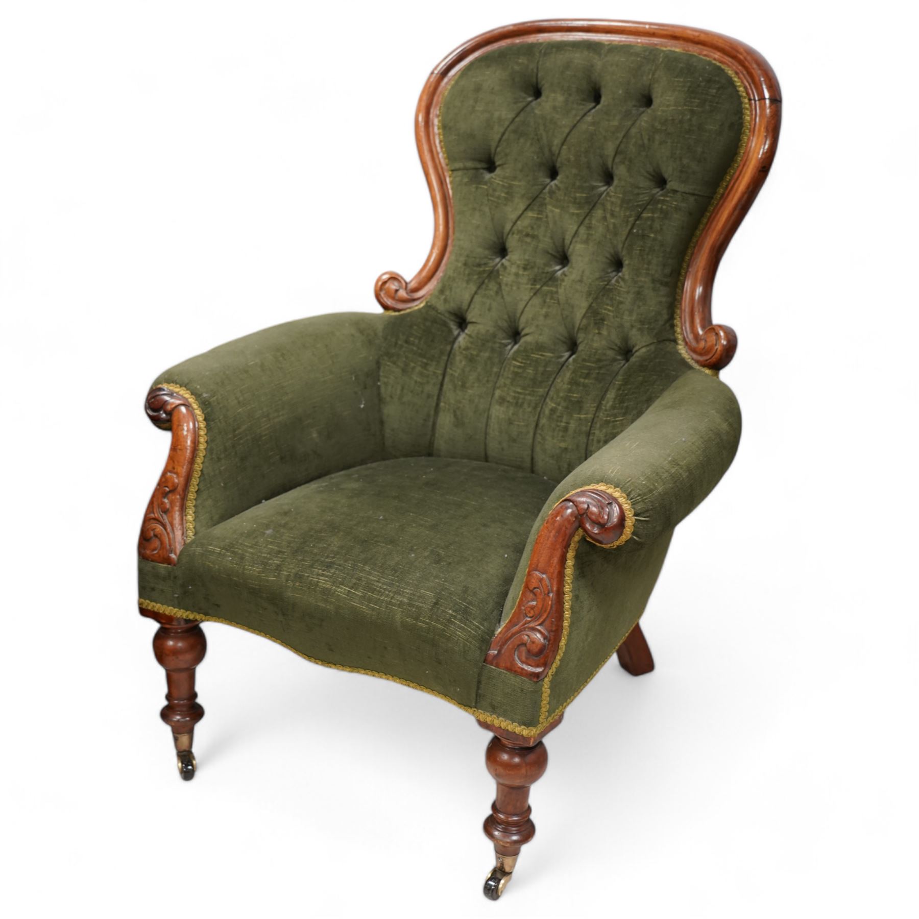 Victorian mahogany spoonback armchair, moulded frame with scroll carved terminals, upholstered in buttoned green fabric, rolled arms with foliage scroll carved facias, on turned front feet with brass cups and castors 