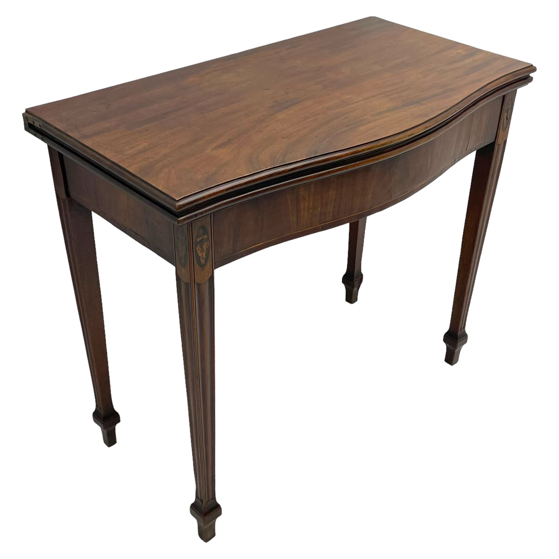 George III inlaid mahogany serpentine card table, the fold-over top with moulded edge supported by gate-leg action, the banded frieze with boxwood stringing, flanked by oval ebony inlay decoration with oak leaf and acorn motifs, raised on fluted supports