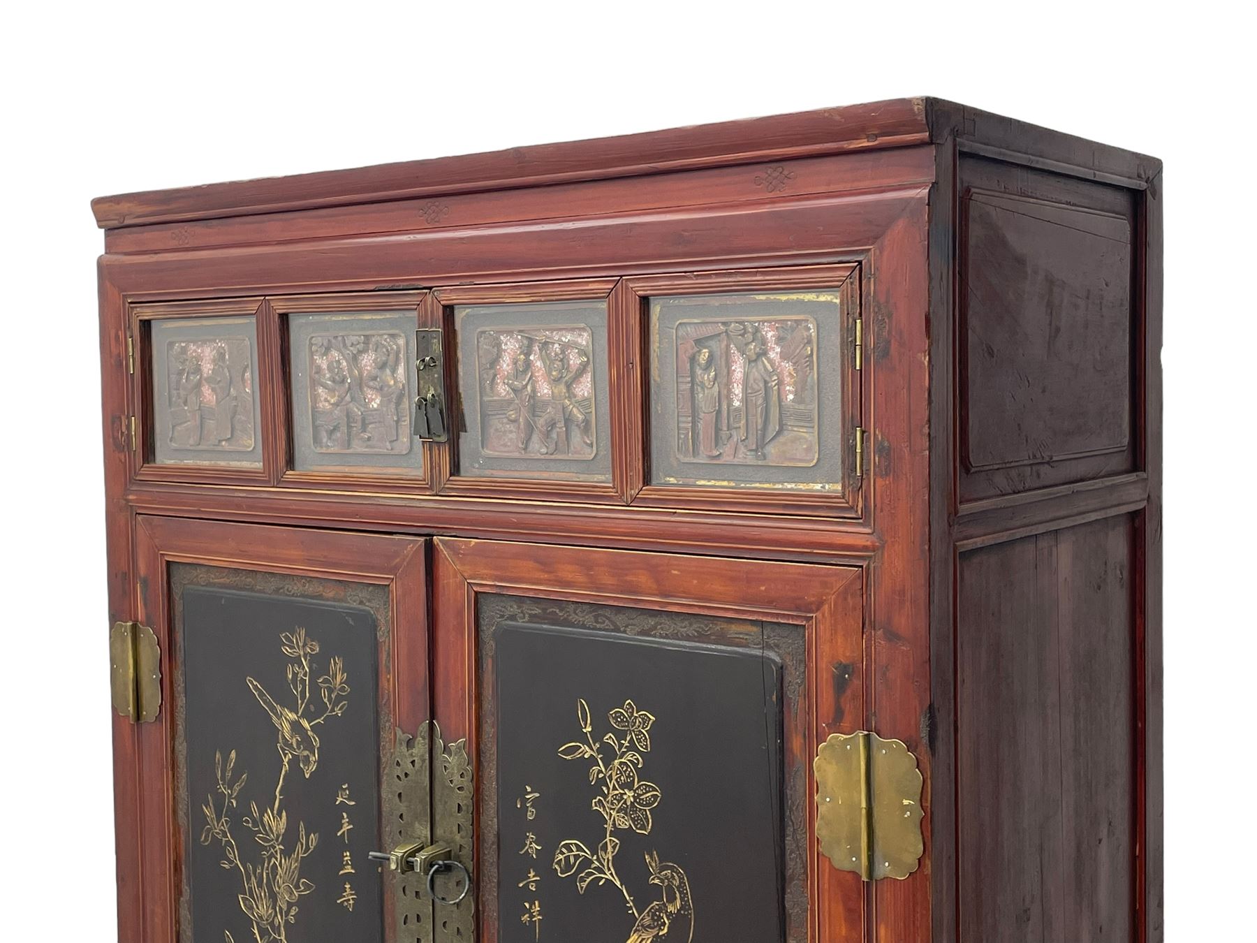 Late 19th century Chinese Qing dynasty red and black lacquered wood cabinet, Fujianese province, upper cupboard enclosed by two doors with relief carved and gilt panels depicting figures behind glass, the large cupboard enclosed by two panelled doors carved with trailing foliate branches and birds, inscribed with Chinese characters, to the left ‘Prolong life’ and to the right ‘Wealth and good fortune’, fitted with two drawers, square supports with carved brackets 