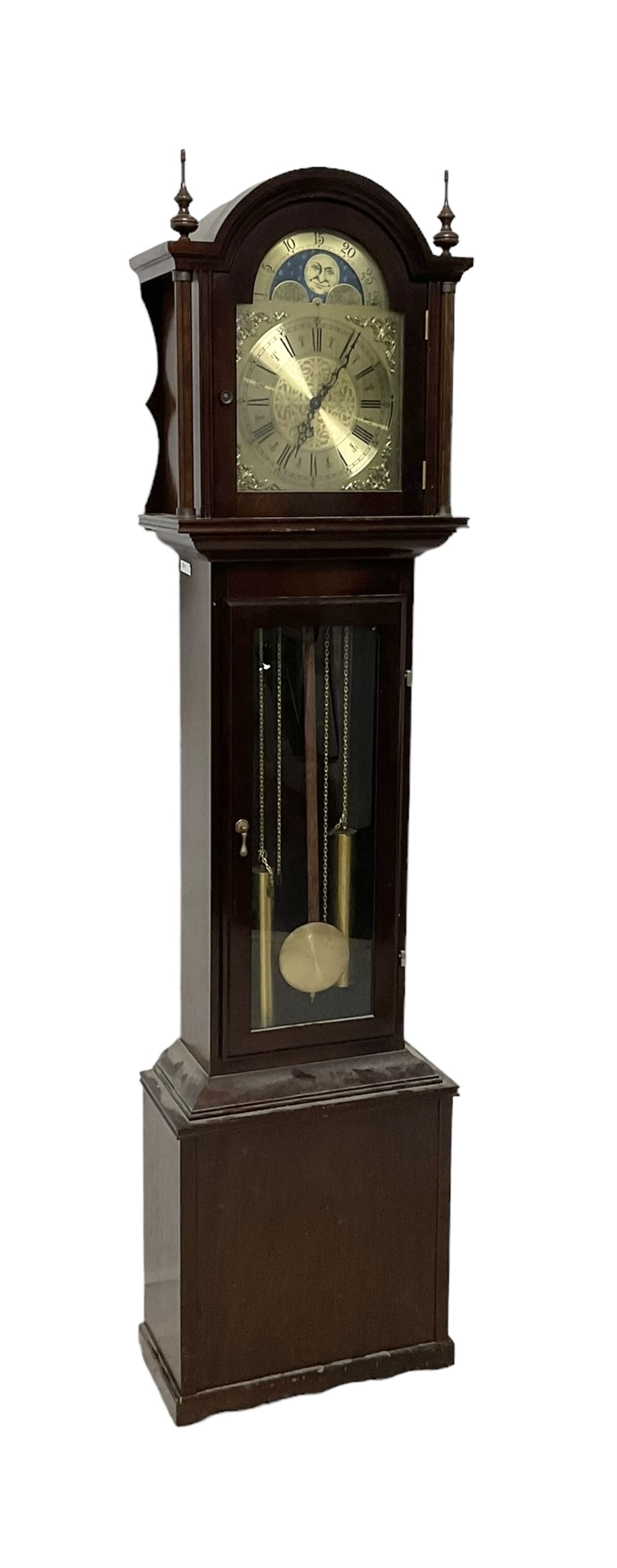 20th century - Westminster chime 8-day grandmother clock in a mahogany case, with a break arch top and brass finials, fully glazed trunk door with visible brass cased weights and pendulum, brass dial with etched dial centre and spandrels, chapter ring with Roman numerals and working moon disc to the arch, two train chain driven movement with 12 gong rods and chime selection for the quarters and hours.