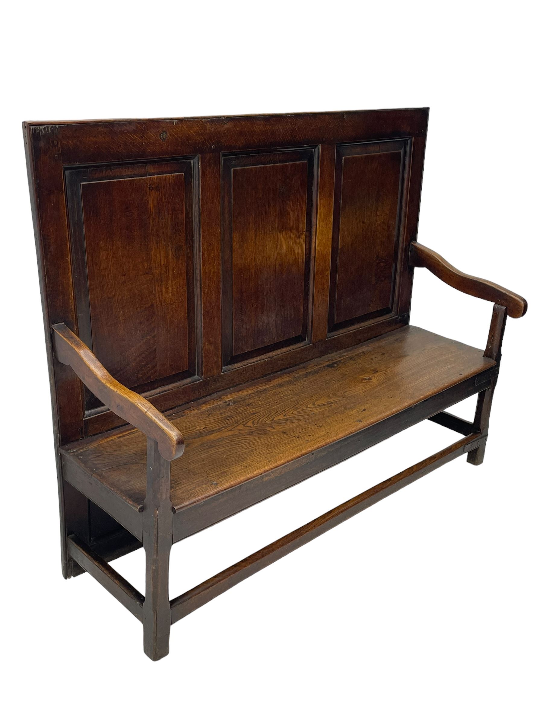 18th century oak settle, the high back with three fielded panels, shaped arms and solid plank seat, standing on square supports joined by stretchers