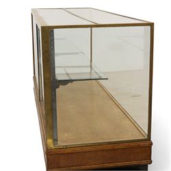 Early 20th century glazed oak and brass bound shop's display cabinet or haberdashery cabinet, fitted with two sliding glass doors, two glass shelves on chromed metal supports, black finish block feet