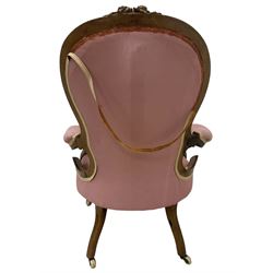 Victorian mahogany framed open armchair, spoon-back and sprung seat upholstered in pink fabric, scrolled arm terminals over serpentine fronted seat decorated with moulded carved floral motifs, cabriole supports with ceramic castors