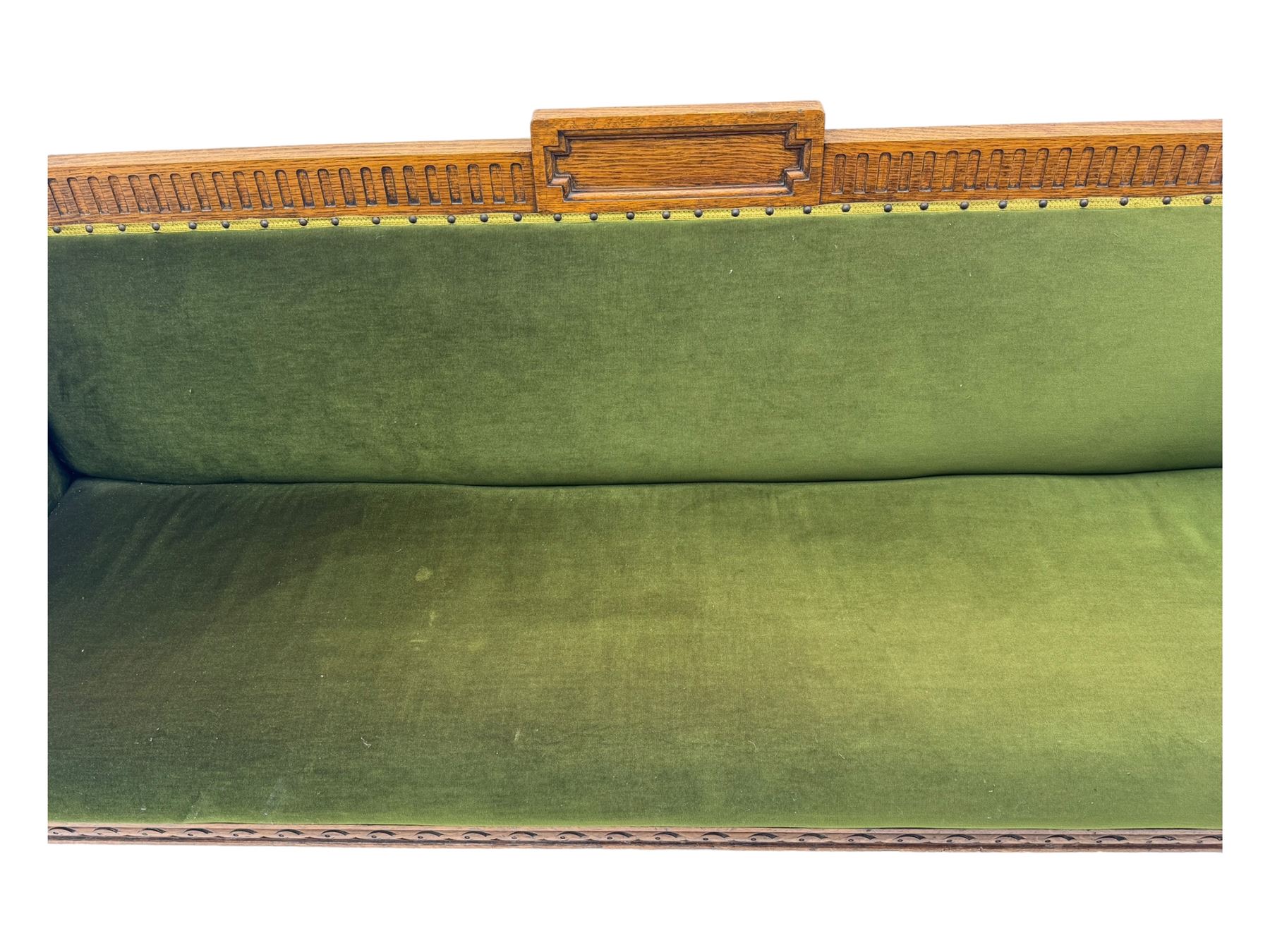 Late Victorian walnut framed sofa, rectangular backrest with carved detailing and central motif, upholstered in olive green fabric with brass studded trim and patterned front rail, scrolled fluted arms supported by turned uprights terminating in bun feet