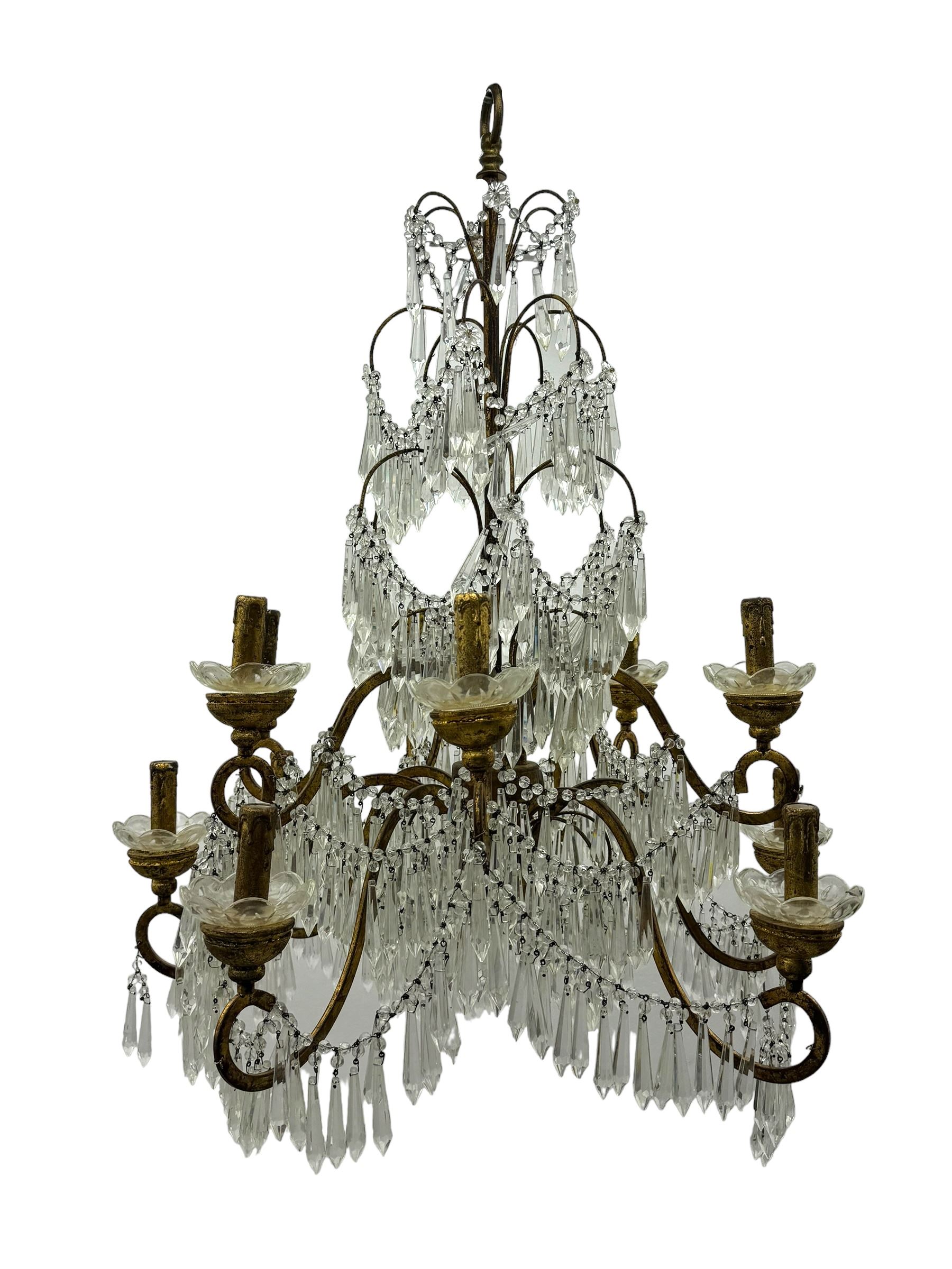 India Jane Interiors - pair of contemporary gilt bronze and crystal chandeliers, the framework featuring scrolling arms and garlands of crystal beads, each with twelve candle-style light fixtures with scalloped glass bobeches, adorned with multiple tiers of cut glass prisms, terminating in a central finial with a suspension loop