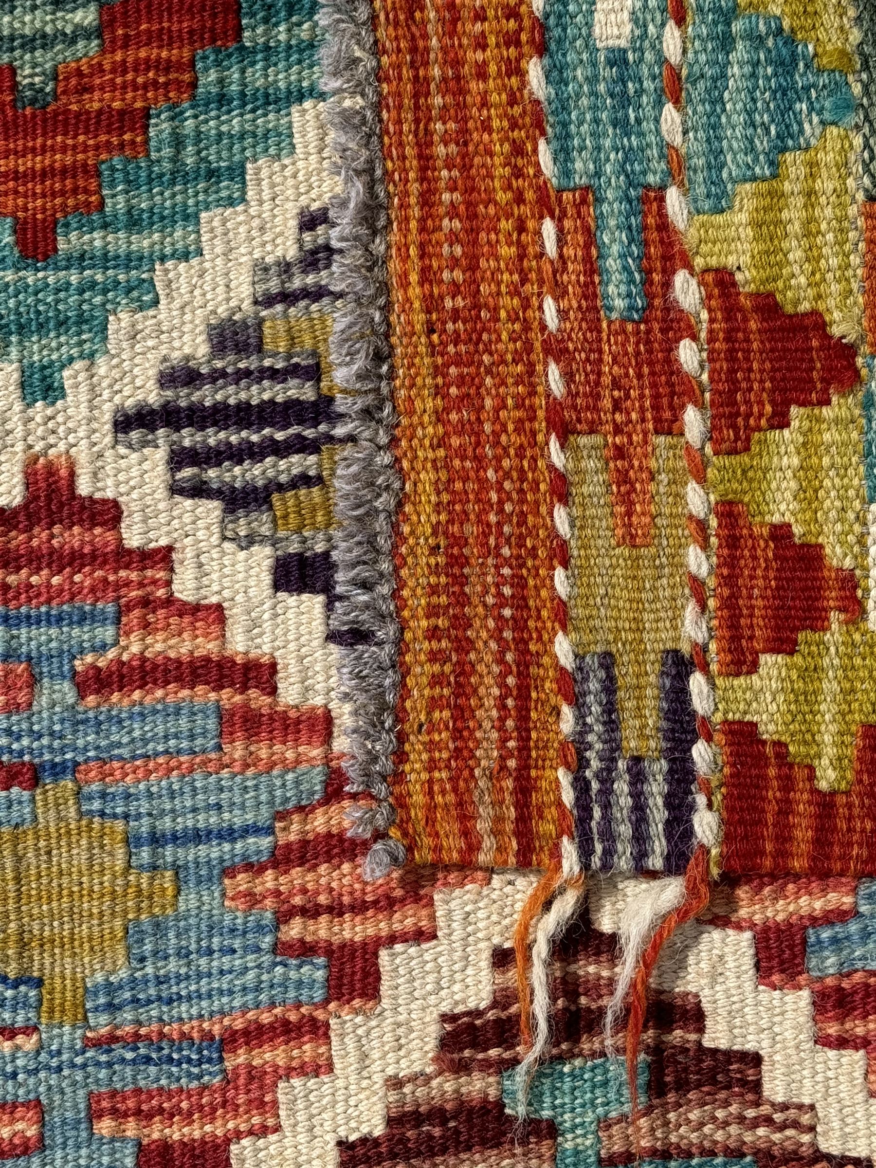 Chobi Kilim ground runner, the field decorated with a geometric pattern of coloured diamonds and triangles, each containing stylised motifs, the shorter ends enclosed by a plain border, and the longer sides with a multicoloured border

