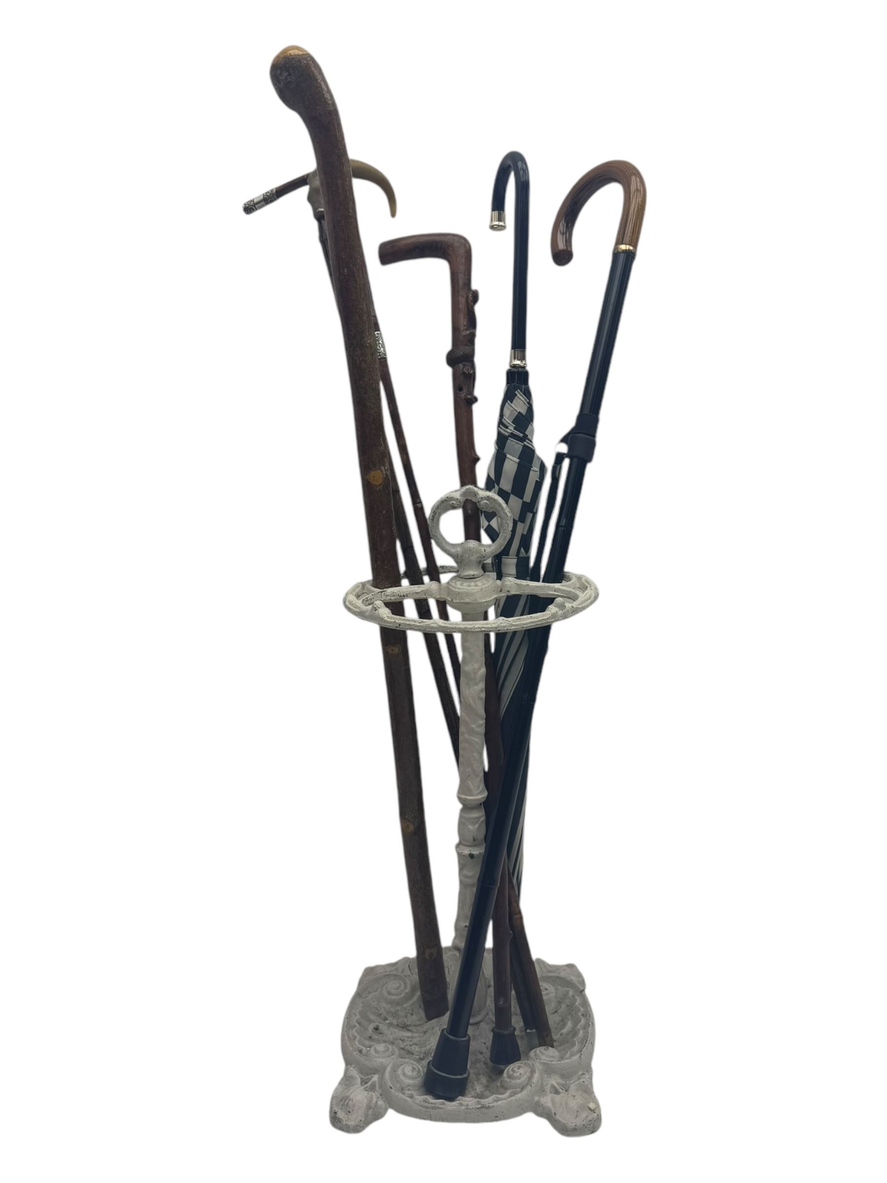 Victorian design cast iron umbrella stand, ornate stem on shell C-scroll base; together with a collection of walking sticks including a silver tipped cane 