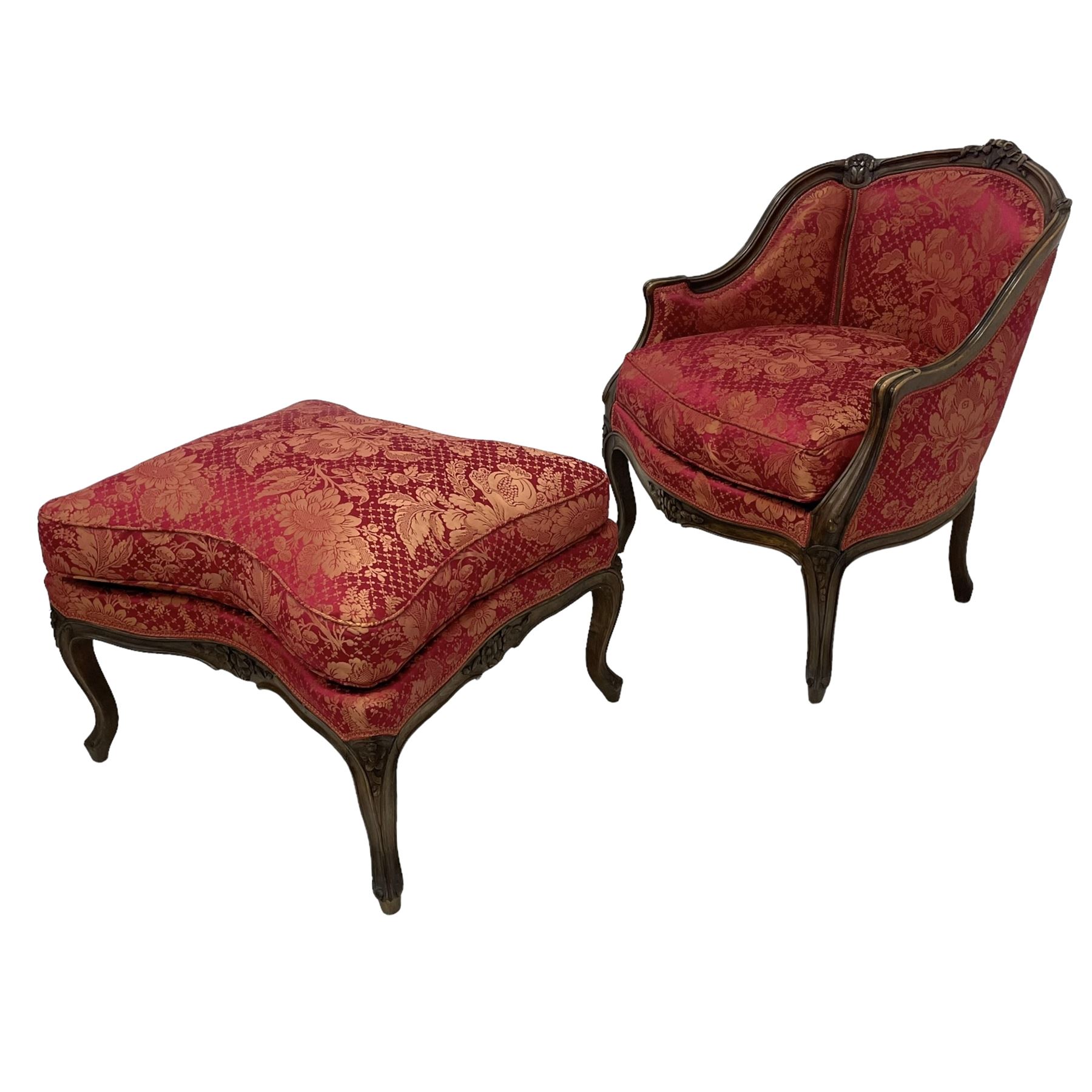 Late 20th century French design stained beech framed armchair and matching stool - the armchair with shaped and moulded frame carved with flower heads and foliage, upholstered in silk red and gold ground fabric with floral pattern, on scroll carved cabriole feet decorated with flower head carvings (W73cm, H82cm, D75cm); the footstool of concaved rectangular form with moulded frame carved with flower heads, upholstered loose cushion, on cabriole feet (70cm x 64cm, H48cm)