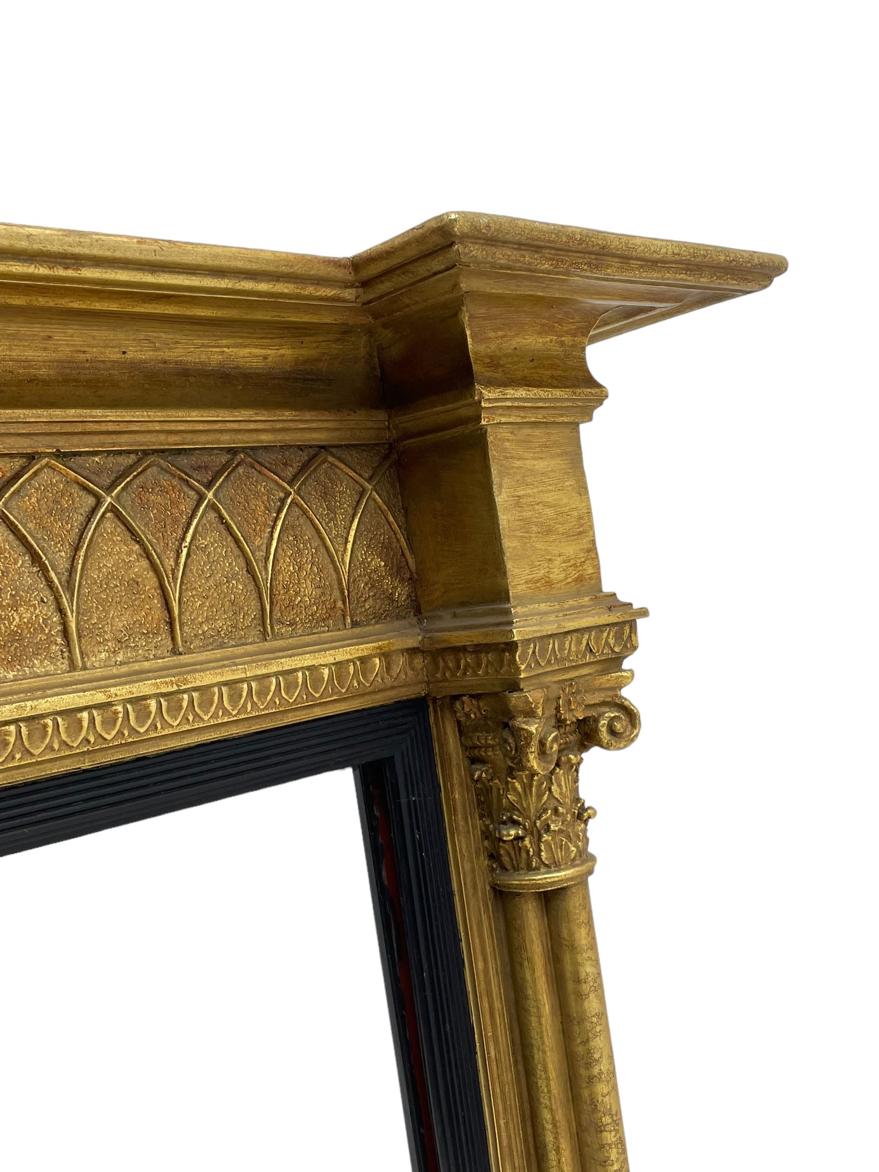 Regency design giltwood overmantel mirror, projecting cornice over pointed arcade frieze and foliate moulded upper edge, plain mirror plate within reed moulded ebonised slip, flanked by cluster columns with acanthus and scroll decorated Composite order capitals 