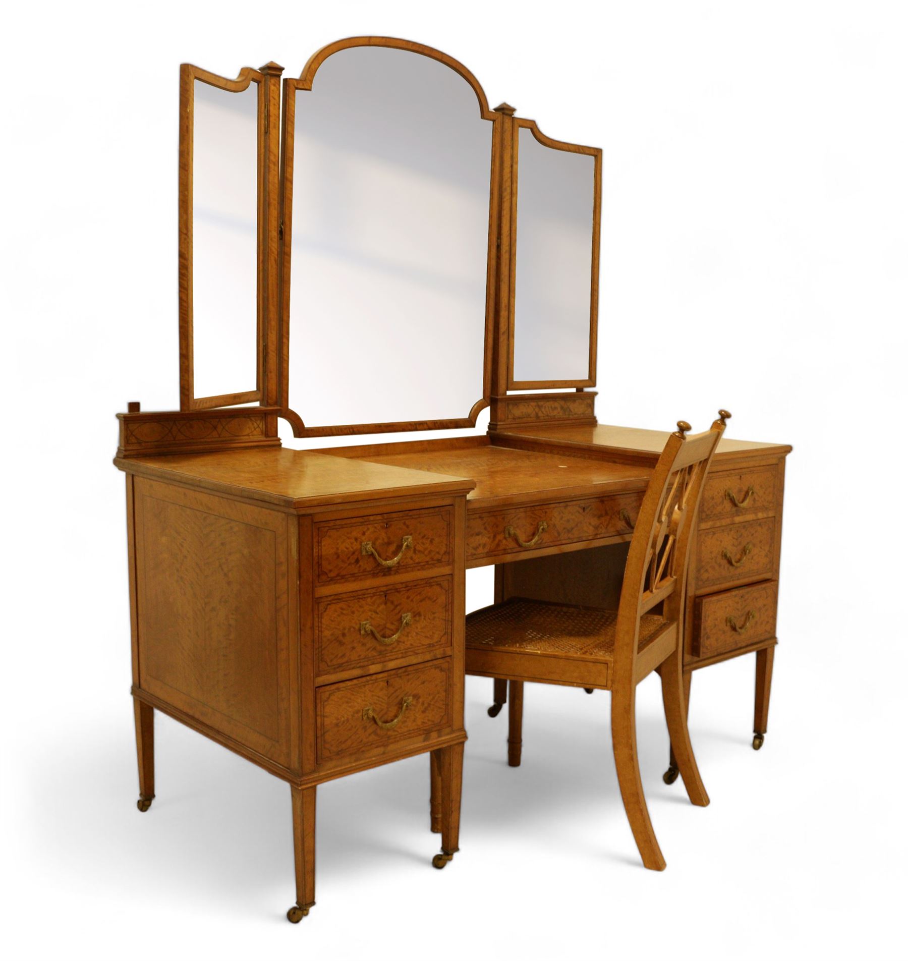 Waring & Gillow Ltd. - Edwardian satinwood dressing table, raised bevelled triple mirror back on square supports, over frieze inlaid with geometric stringing in ebony, moulded drop-centre table with stringing, fitted with seven drawers, reeded and foliate cast handles and square leaf cast handle plates, on square tapering supports terminating to brass castors, the centre drawer with metal maker's plaque and maker's stamp for 'Waring & Gillow, Ltd.', the top three drawers fitted with Chubb locks, the remaining drawers fitted with locks stamped 'Gillows Lancaster', together with associated chair 