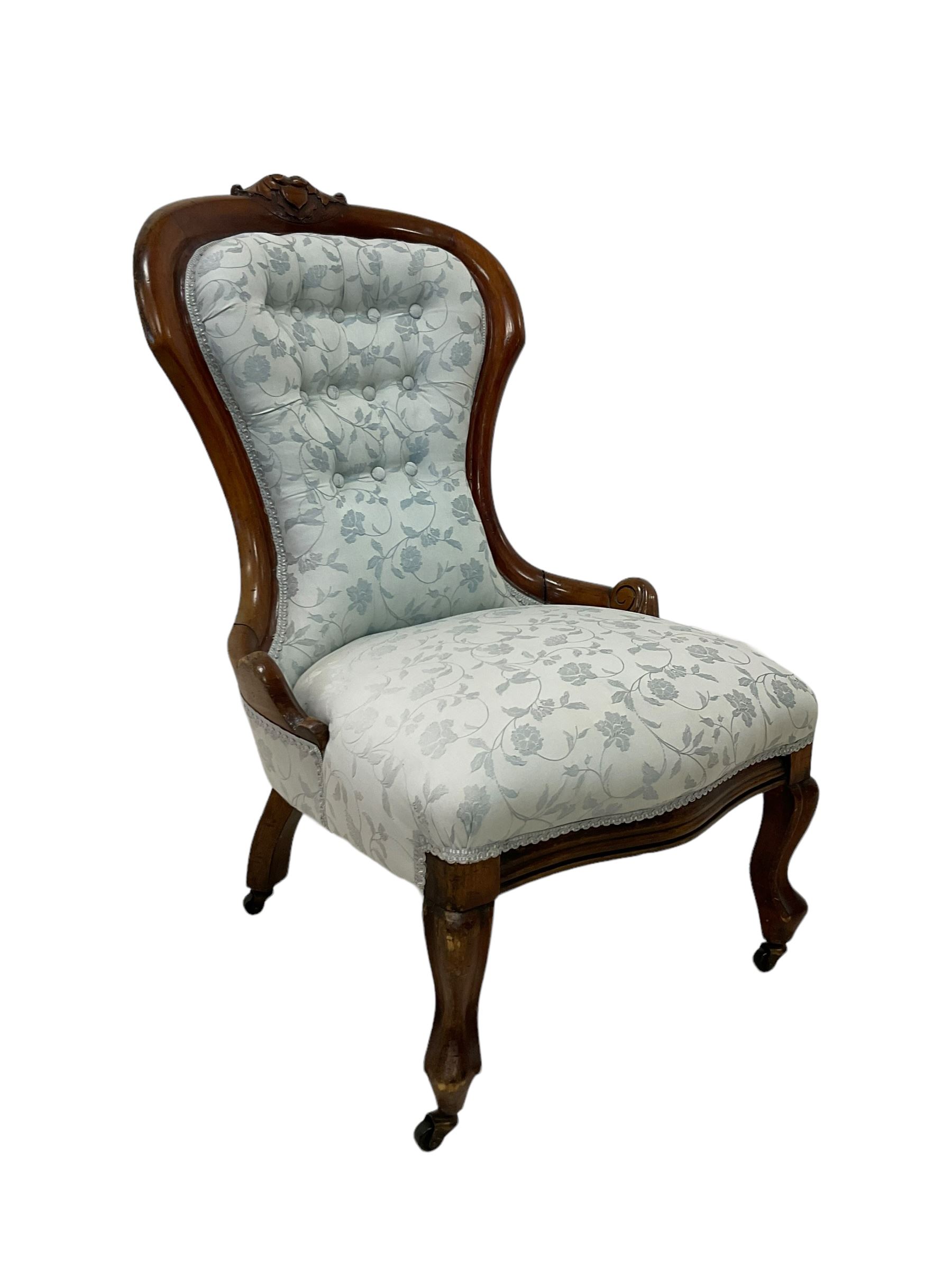 Victorian walnut nursing chair, the curved cresting rail carved with central cartouche and scroll leaves, upholstered in pale blue fabric decorated with trailing floral design, on cabriole front feet 