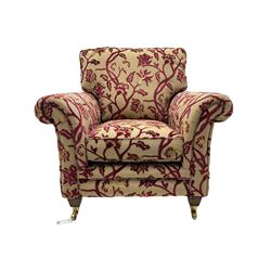 Contemporary upholstered armchair, scroll arms and loose cushions, embossed beige ground fabric with red and gold floral motifs, on tapered wooden supports with front brass castors