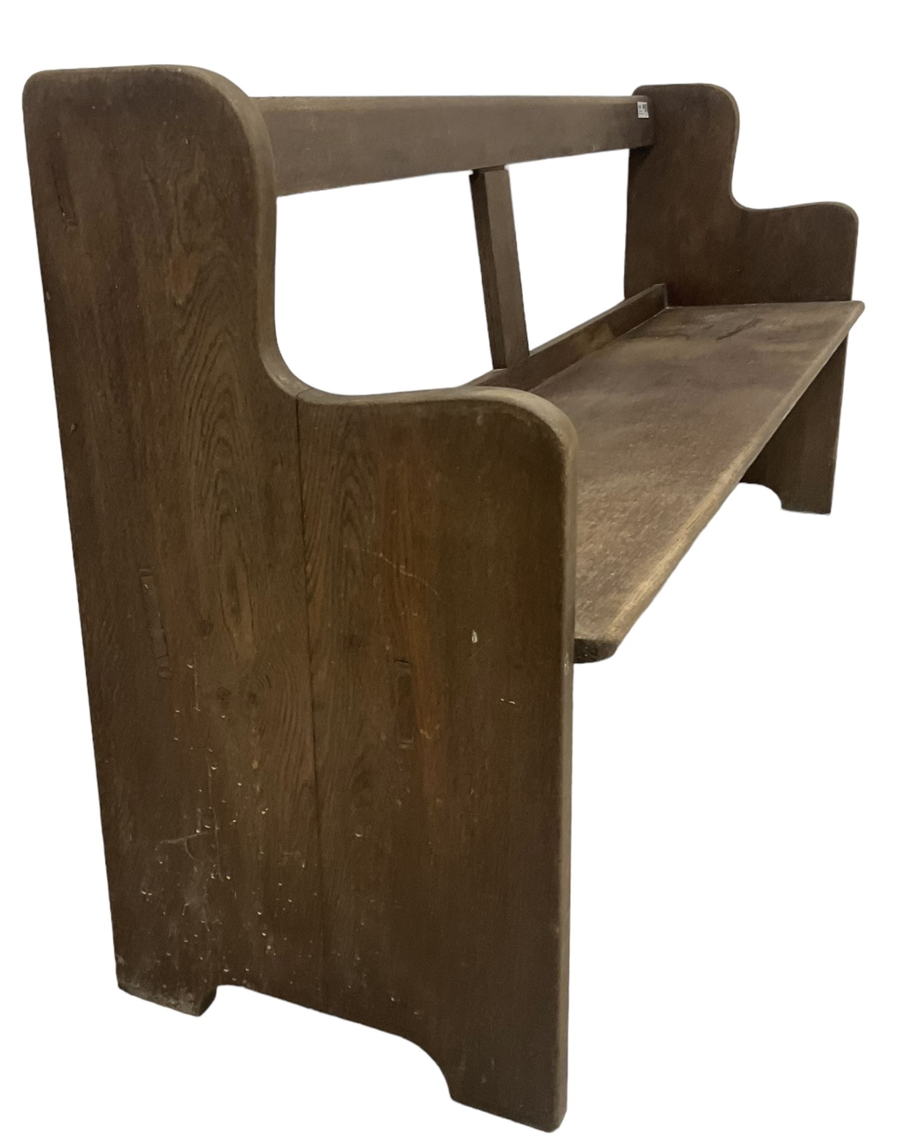 Early 20th century oak church pew or hall bench, open back over single plank seat, on shaped end supports