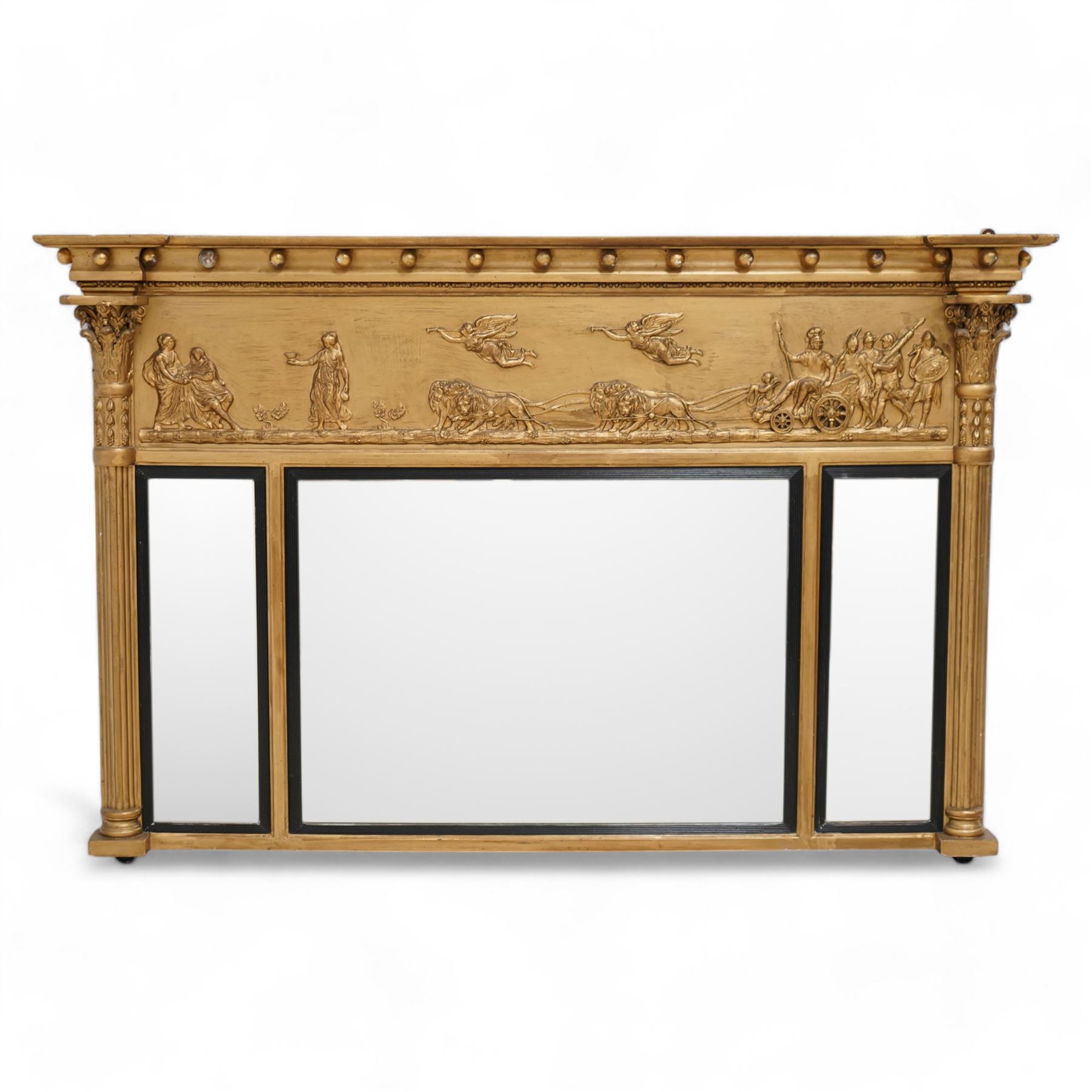 Regency gilt overmantle mirror, inverted breakfront pediment decorated with applied gilt spheres, the relief frieze depicting Magna Mater in her lion-pulled chariot with trumpet playing winged deities overhead, Roman heroes to the back of her with maidens performing rites in front, flanked by half reeded pilasters with Ionic and Corinthian composite capitals, the triple bevelled rectangular plates enclosed by reeded ebonised slips