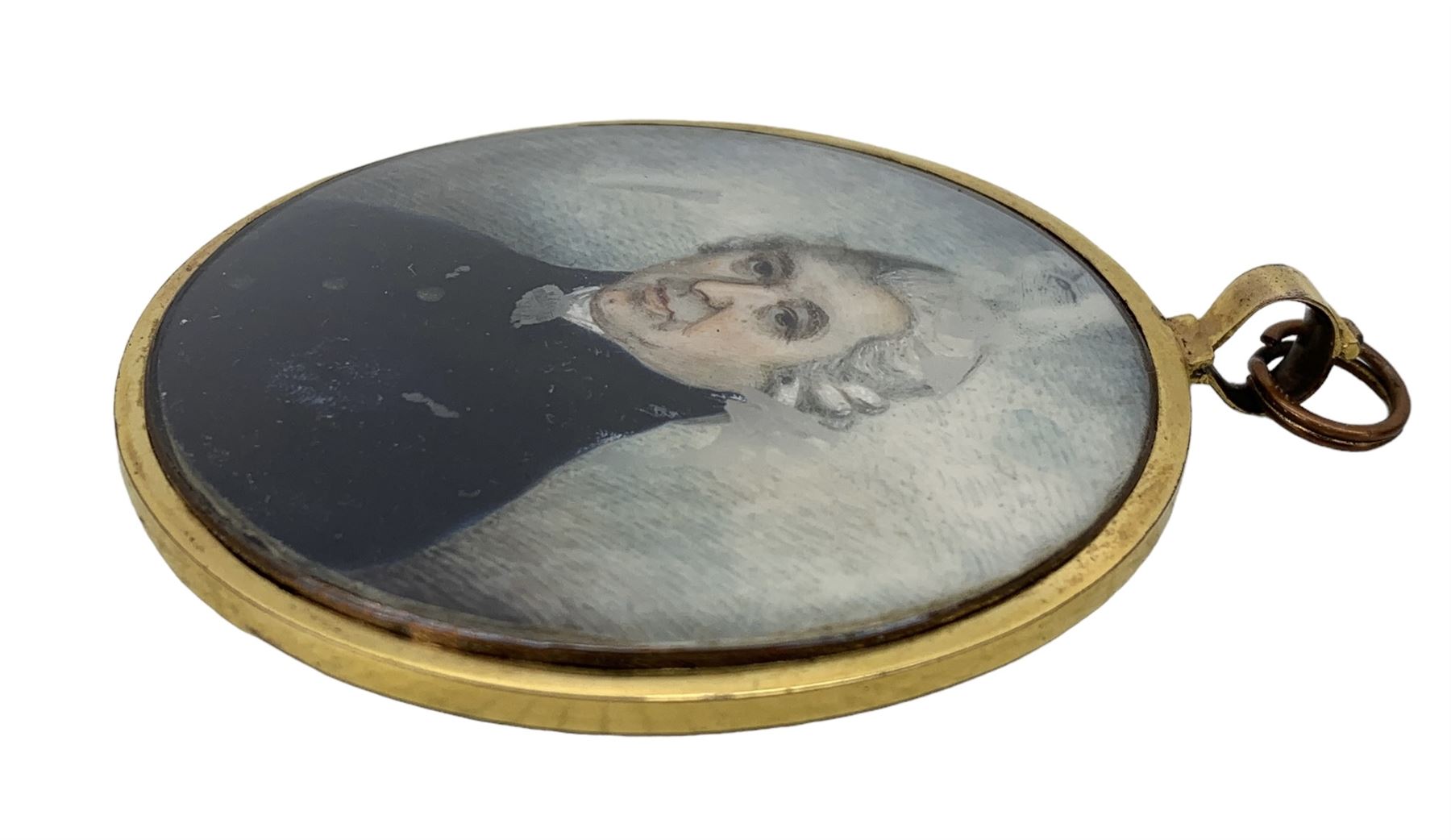 English School (18th/ early 19th century): Miniature portrait of a Gentleman, head & shoulder length, watercolour on ivory, unsigned, the reverse with blue guilloche enamel border and engraving of a gentleman, within an oval brass frame, 6.5cm x 5.5cm. This item has been registered for sale under Section 10 of the APHA Ivory Act