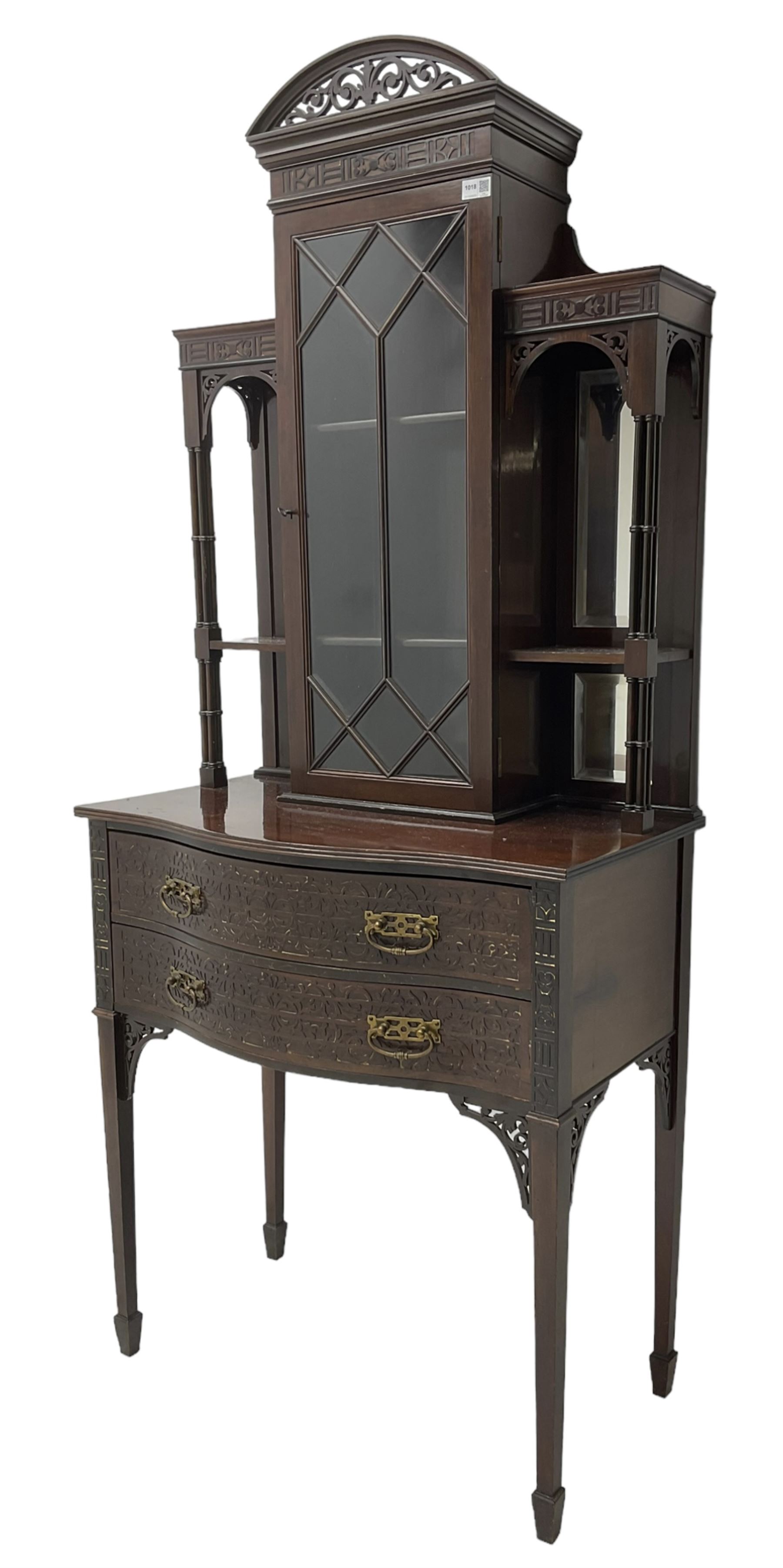 Early 20th century mahogany cabinet on stand, with pierced arched foliate pediment over blind-fretwork frieze, fitted with single astragal glazed door flanked by bevelled mirror back shelves with cluster column uprights, serpentine base fitted with two drawers with blind-fretwork facias 