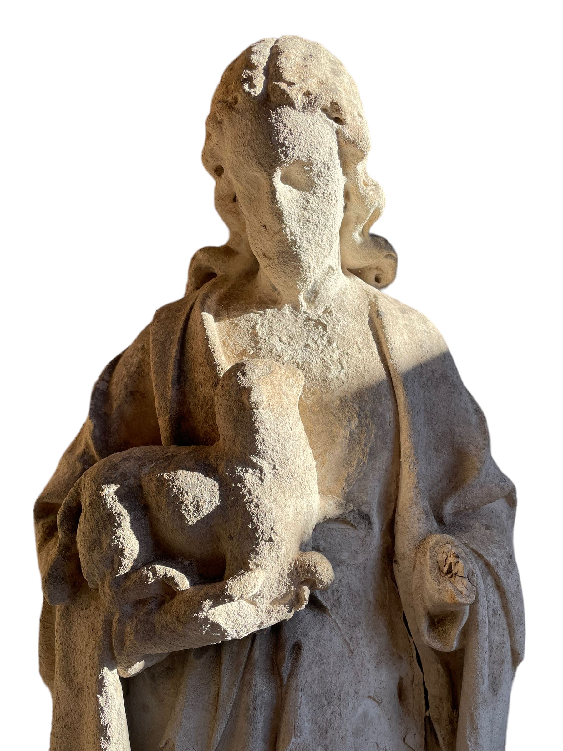 19th century weathered carved sandstone figure of Jesus Christ depicted as the Good Shepherd, draped in robes and holding a lamb, on a naturalistic base