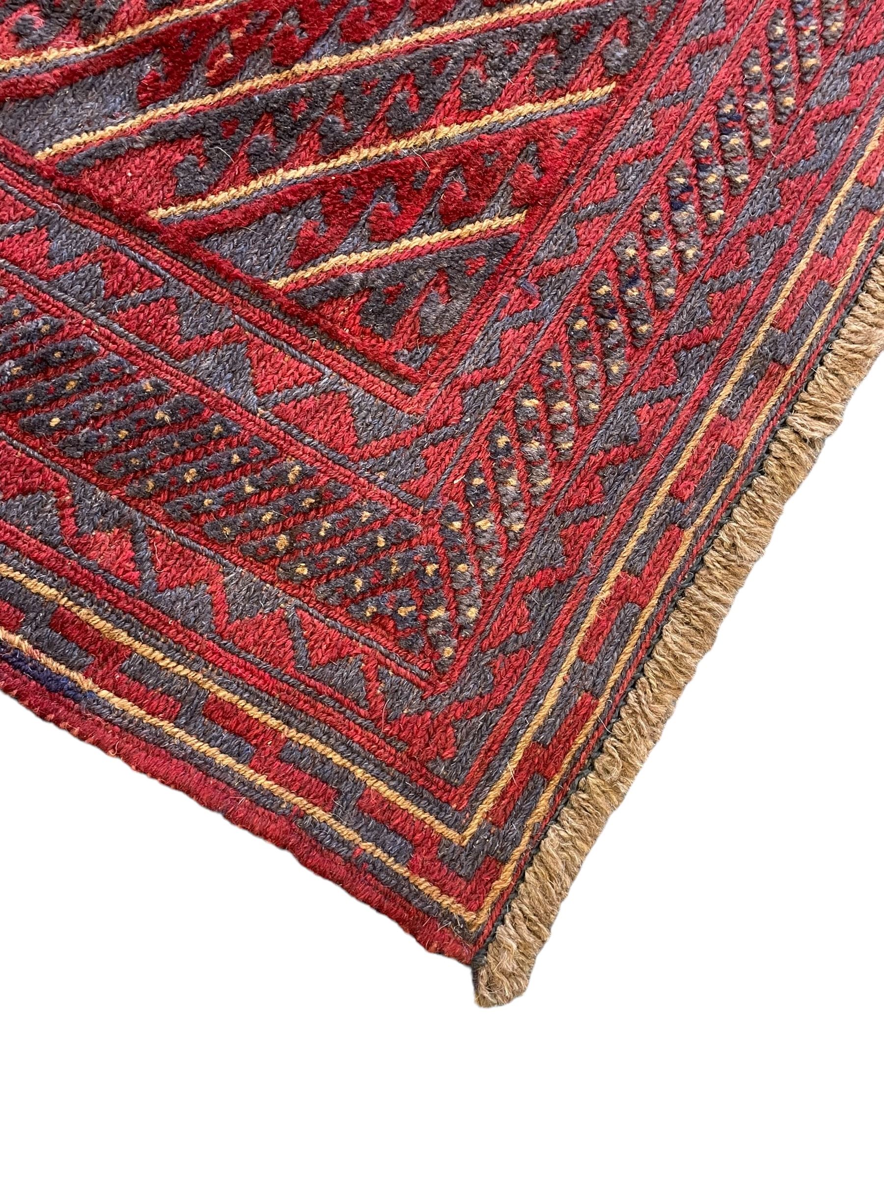 Meshwani indigo and maroon ground rug, the field decorated with a central lozenge with concentric borders containing hook motifs, enclosed by geometric zig-zag guard lines