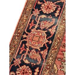 Persian Heriz design rug with red ground, the field featuring a central medallion with floral and geometric motifs, surrounded by ivory spandrels, the main border showcasing a series of floral patterns on a dark blue ground