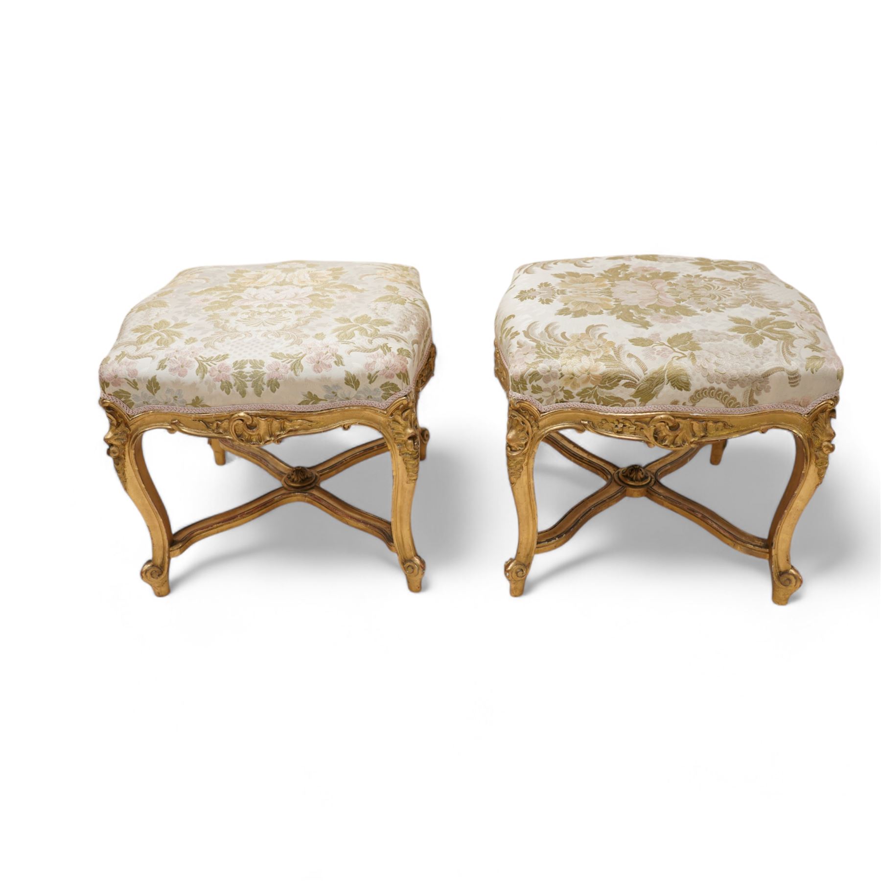 James Shoolbred & Co. (London: 1814-1934) - pair of late 19th century giltwood French design stools, shaped seat upholstered in floral pattern fabric, on shell carved cabriole supports with scrolled terminals, united by shaped X-frame stretchers, with ivorine maker's label inscribed 'Jas Shoolbred & Co.' 