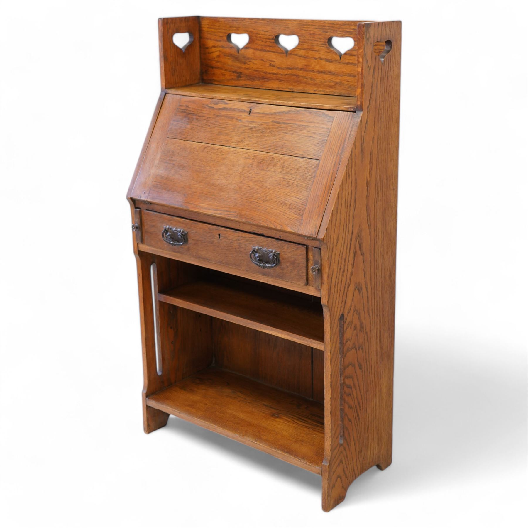 Possibly Liberty & Co - Arts & Crafts light oak bureau, the three-quarter raised gallery pierced with hearts, over a fall-front enclosing fitted interior with correspondence and pigeonholes, fitted with single drawer with poppy decorated handles, single open shelf to base