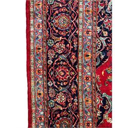 Persian Kashan crimson ground carpet, central rosette medallion on a field of trailing foliate branches decorated with palmettes, scrolling border with repeating plant motifs and flower heads, enclosed within floral pattern guard stripes