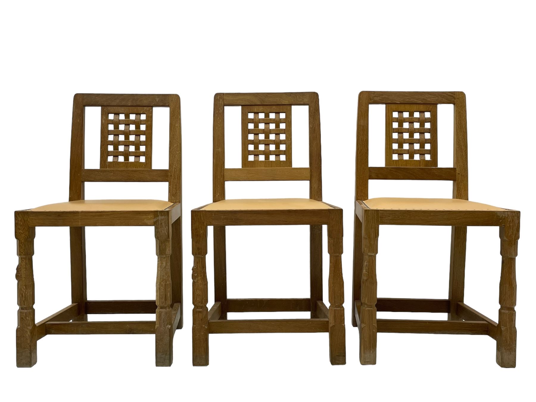 Mouseman - set of six oak dining chairs, pierced and carved lattice panel back over tan leather seat with studded band, on octagonal front supports united by plain H stretchers, carved with mouse signature, by the workshop of Robert Thompson, Kilburn 