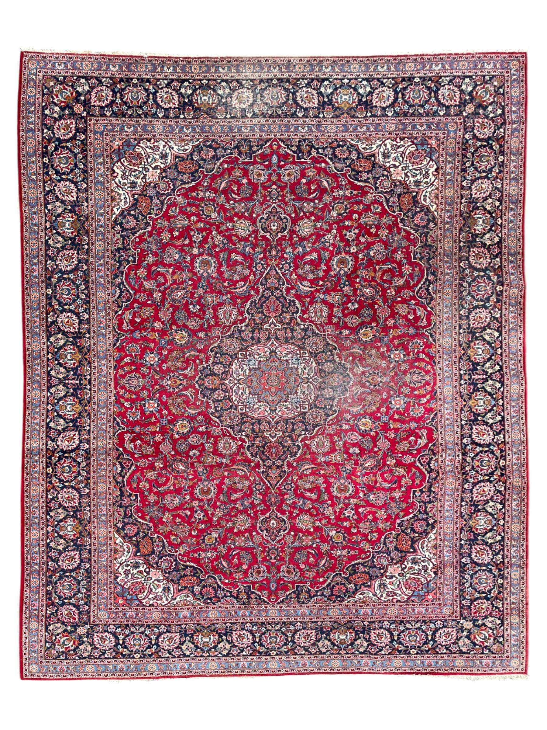 Large Persian Kashan crimson ground carpet, central floral medallion surrounded by swirling leafy branches and palmettes, enclose by floral pattern spandrels, the indigo border with overall scrolling design decorated with palmettes, within guard stripes 