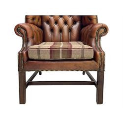 Georgian design hardwood-framed wingback armchair, shaped cresting rail and deep wingback over rolled arms, upholstered in brown buttoned leather with studwork bands, the seat cushion upholstered in checkered fabric, on square supports united by stretchers (W86cm, H118cm, D86cm); together with matching rectangular footstool (63cm x 43cm, H37cm) 