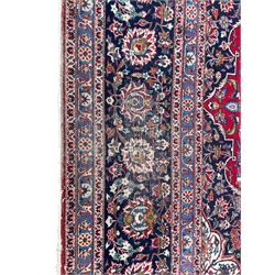 Large Persian Kashan crimson ground carpet, central floral medallion surrounded by swirling leafy branches and palmettes, enclose by floral pattern spandrels, the indigo border with overall scrolling design decorated with palmettes, within guard stripes 