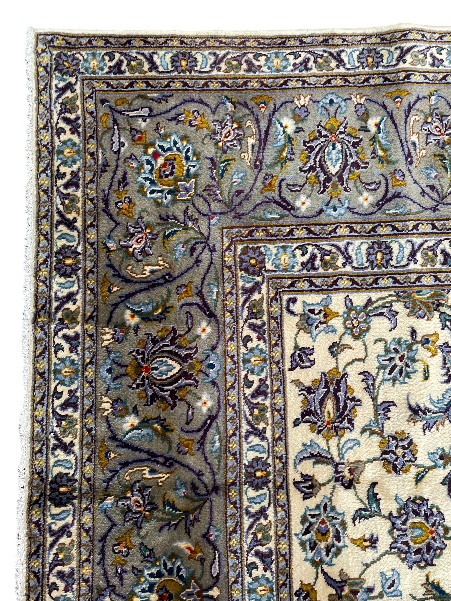 Persian Kashan ivory ground carpet, the busy field decorated with scrolling and interlaced leafy branches and palmettes, trailing branch border with repeating stylised plant motifs, within floral pattern guard stripes 