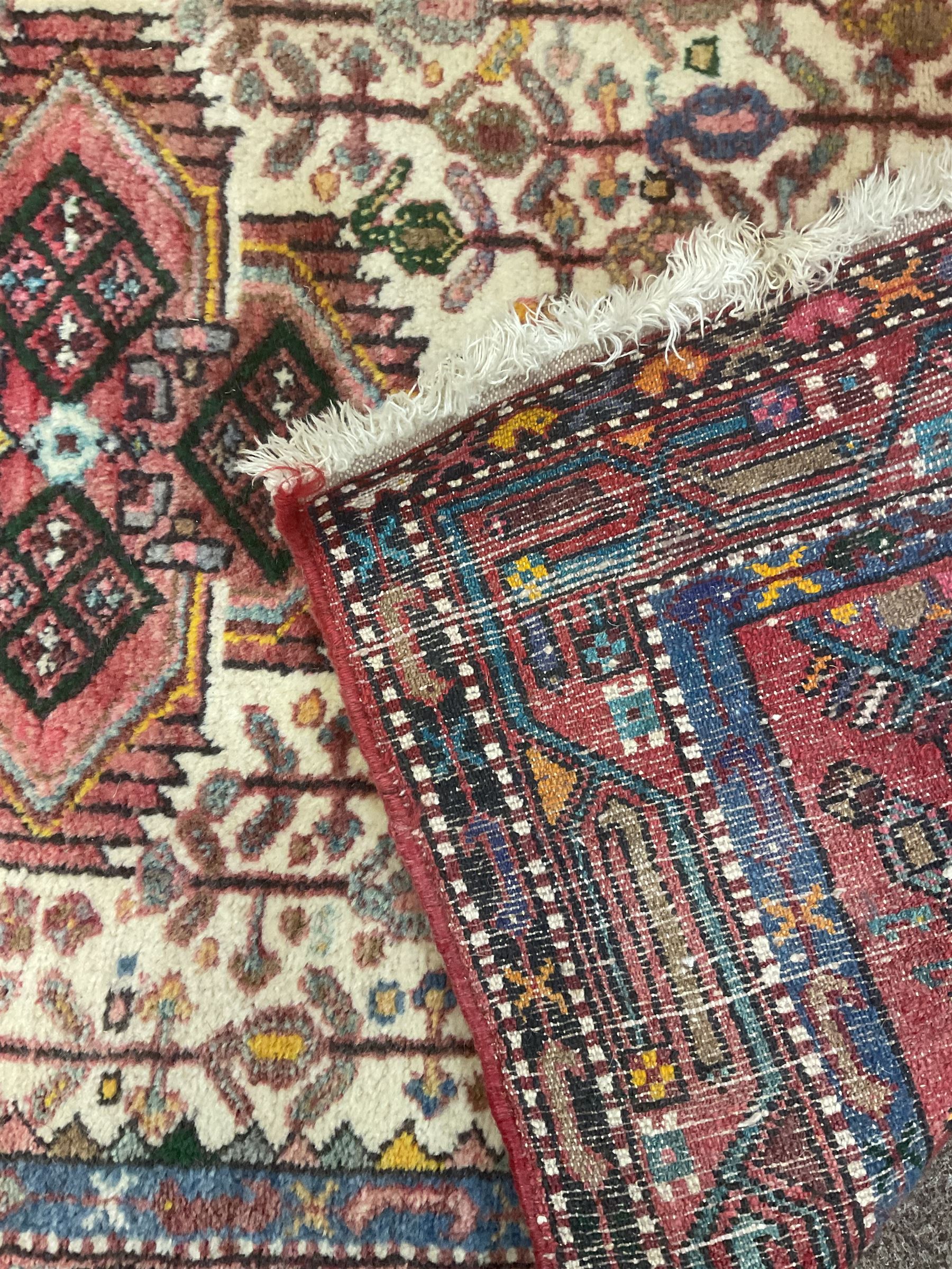 Small Persian rug, ivory and pale red ground, decorated with central medallion within a field of trailing Boteh motifs, geometric design guarded border