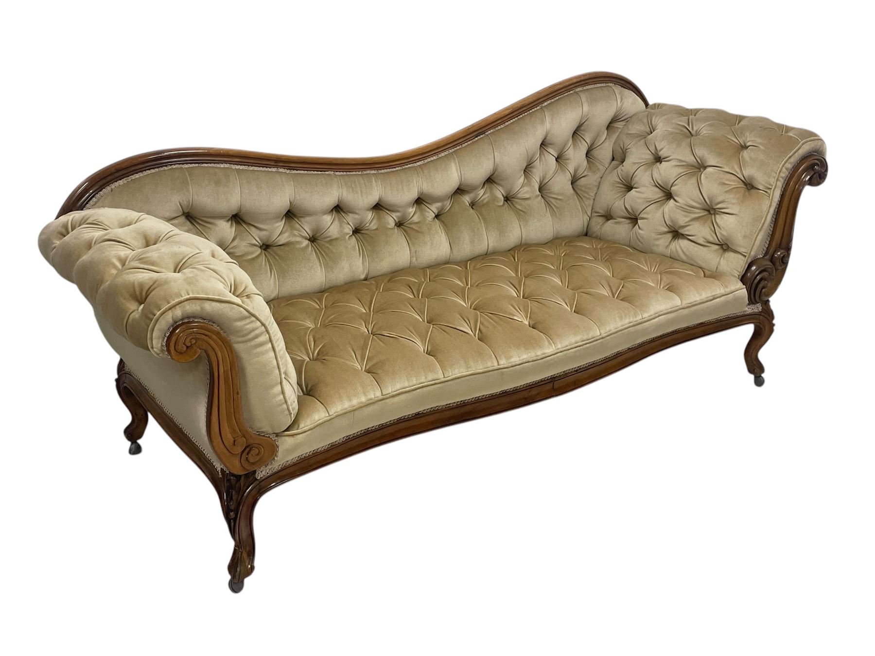 19th century walnut framed chaise longue, shaped back over scrolled arms decorated with moulded curling acanthus carvings, upholstered in deep buttoned champagne fabric, raised on cabriole supports with applied floral carved decoration, on castors