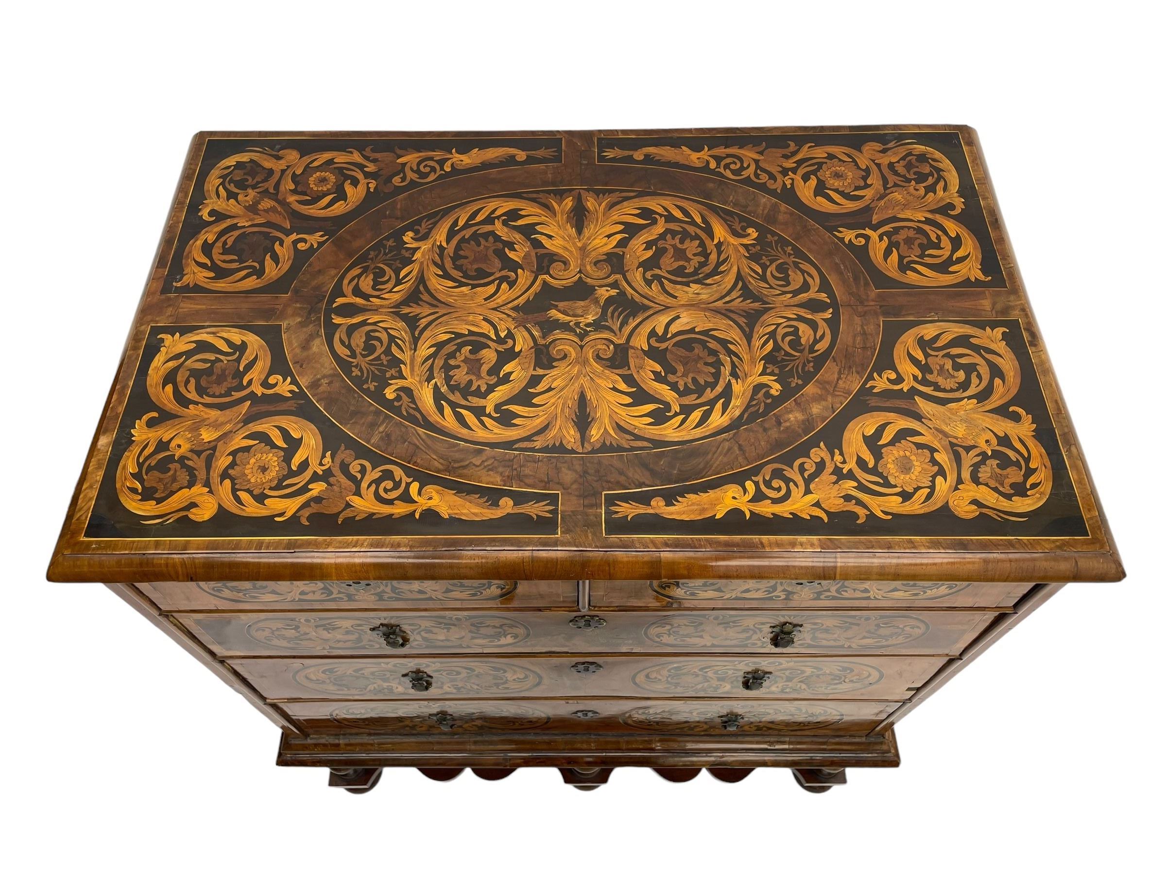 18th century inlaid walnut chest on stand, ovolo-moulded rectangular top inlaid with ebony panels each decorated with scrolling foliage, flower heads and birds, fitted with two short over three long drawers, the drawer fronts decorated with ebony panels enclosing curled leaf inlays, the base fitted with single drawer on turned supports united by waved stretchers, on turned bun feet 