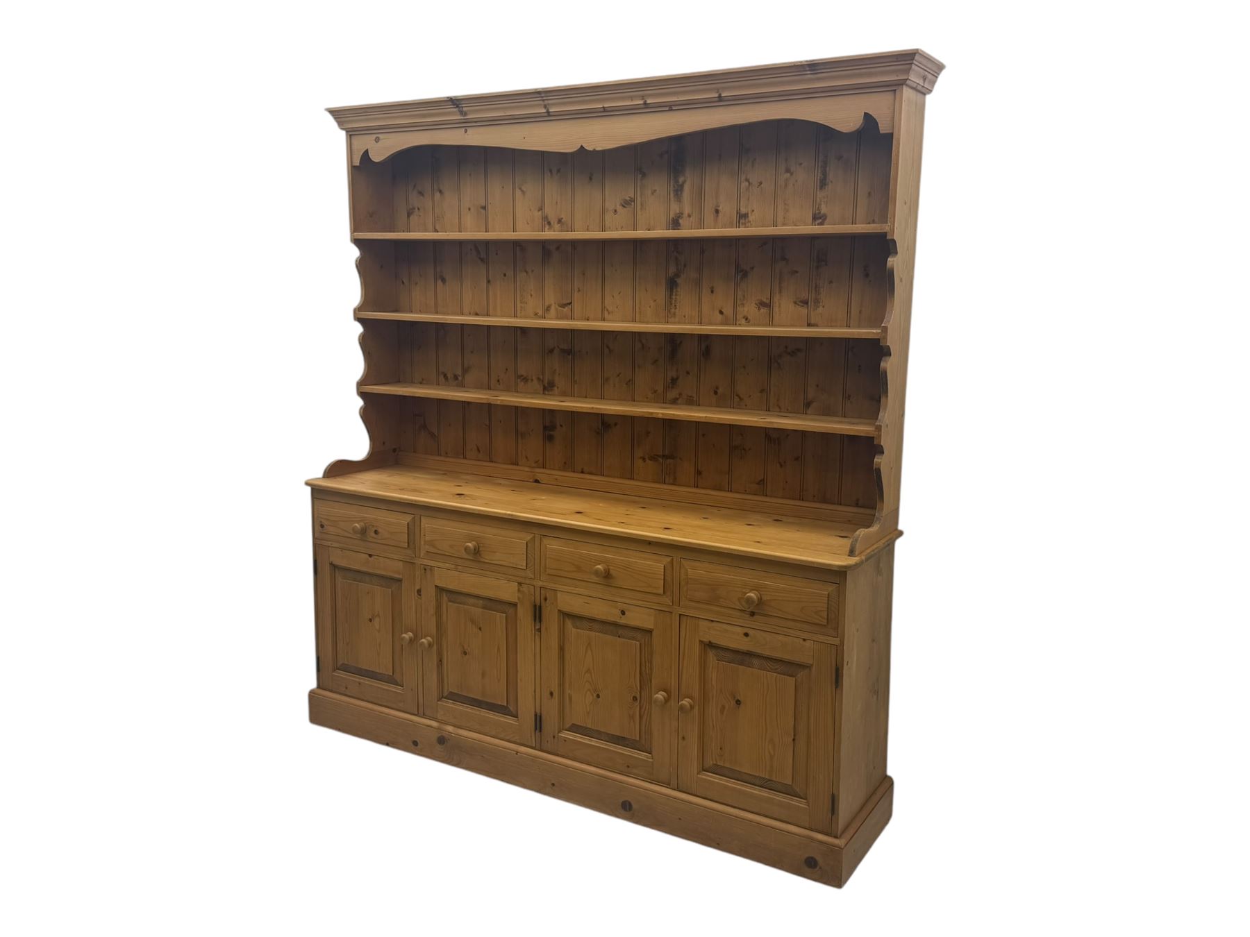 Large traditional pine dresser, shaped cornice over three open shelves, base fitted with four drawers above four panelled cupboards, each with turned wooden knobs, on plinth base