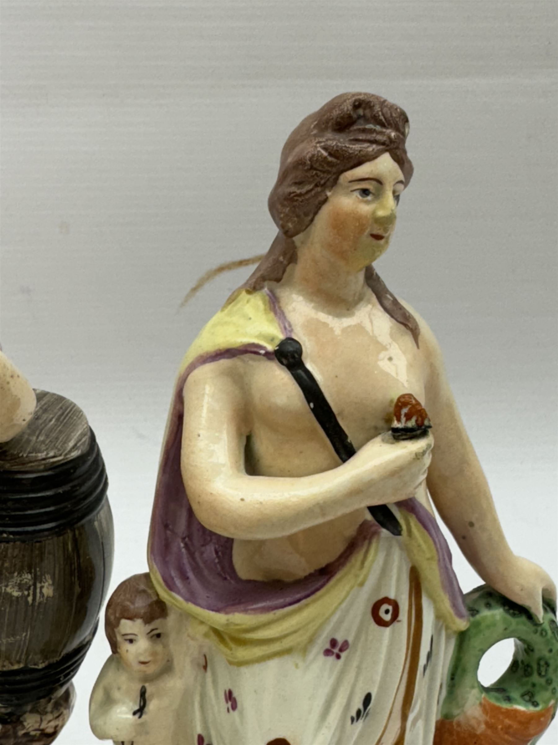 An early 19th Century Staffordshire pearlware figure of The Widow of Zarephath, H23cm, together with another pearlware example modelled as a classical figure in drapery, with putti by side, and supported by a zoomorphic fish to the other wise, H22cm