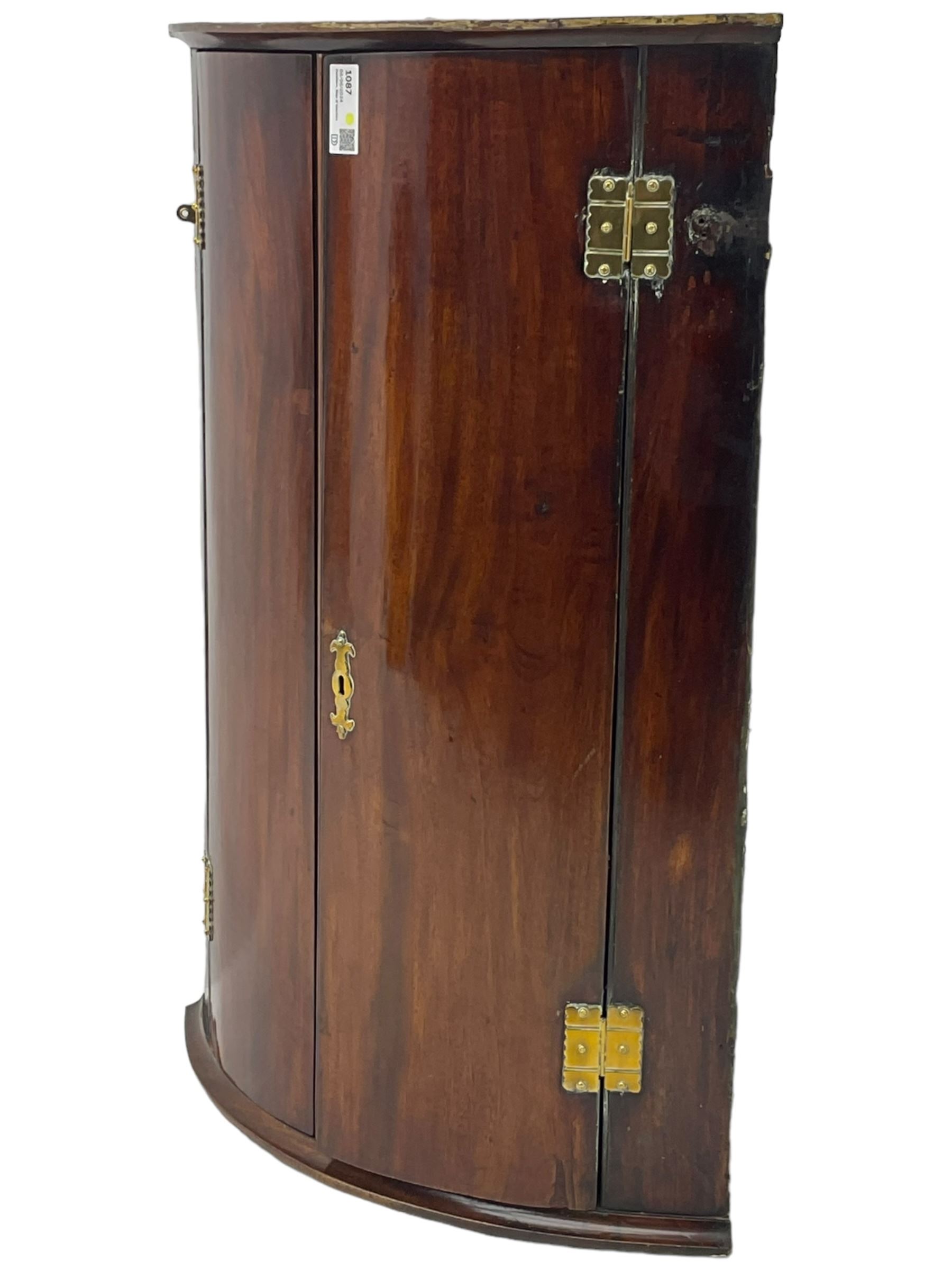 George III mahogany bow-front corner cupboard, enclosed by two figured doors with brass hinges and escutcheon, the painted interior fitted with three shelves 