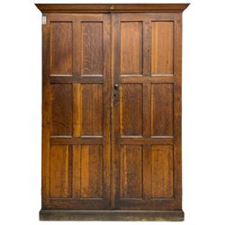 The North of England School Furnishing Company Limited Darlington - early 20th century oak school cupboard, projecting moulded cornice over two panelled doors, fitted with shelves, on chamfered plinth base 